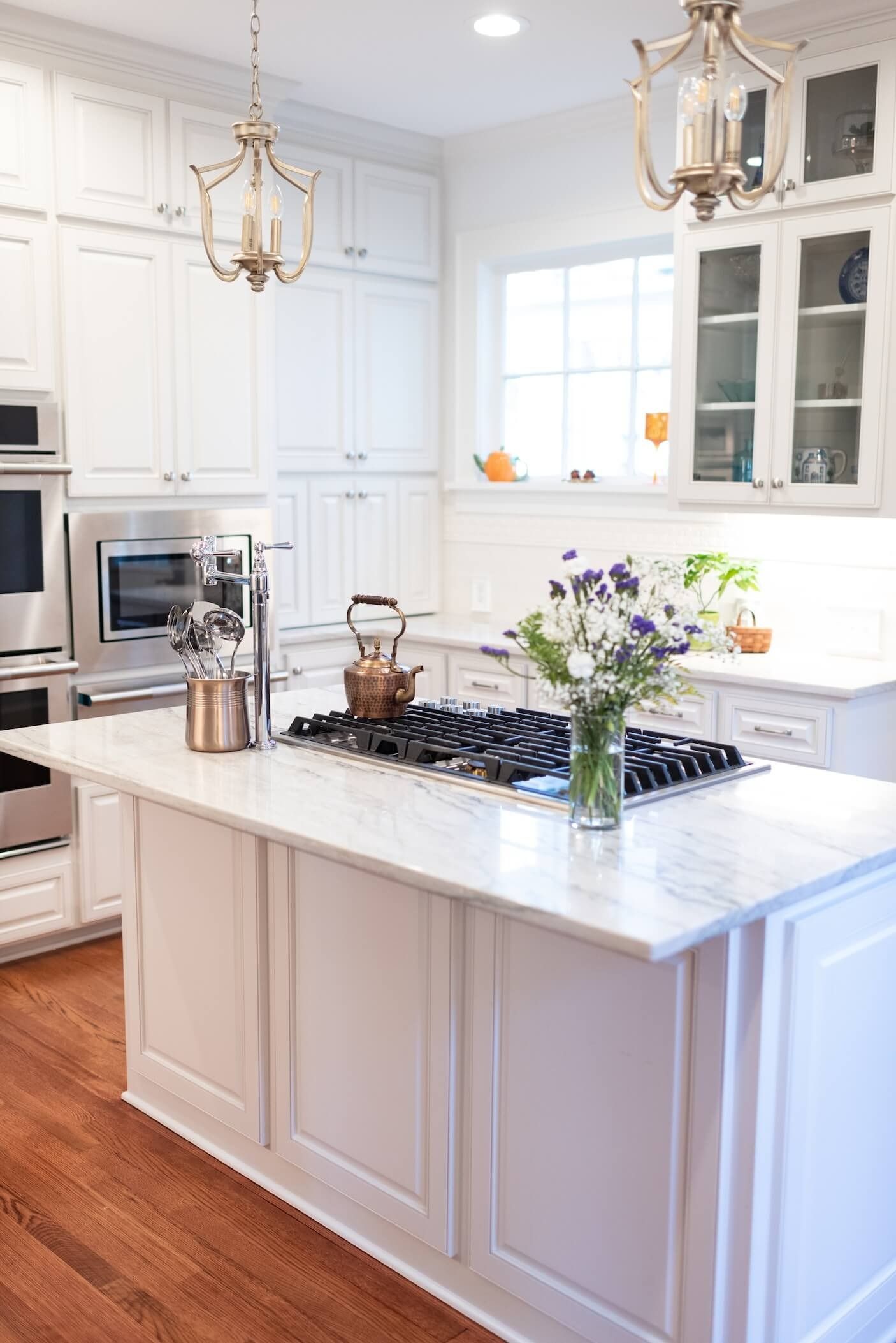 Bright white kitchen with island, gold pendant lights, and flowers on the counter