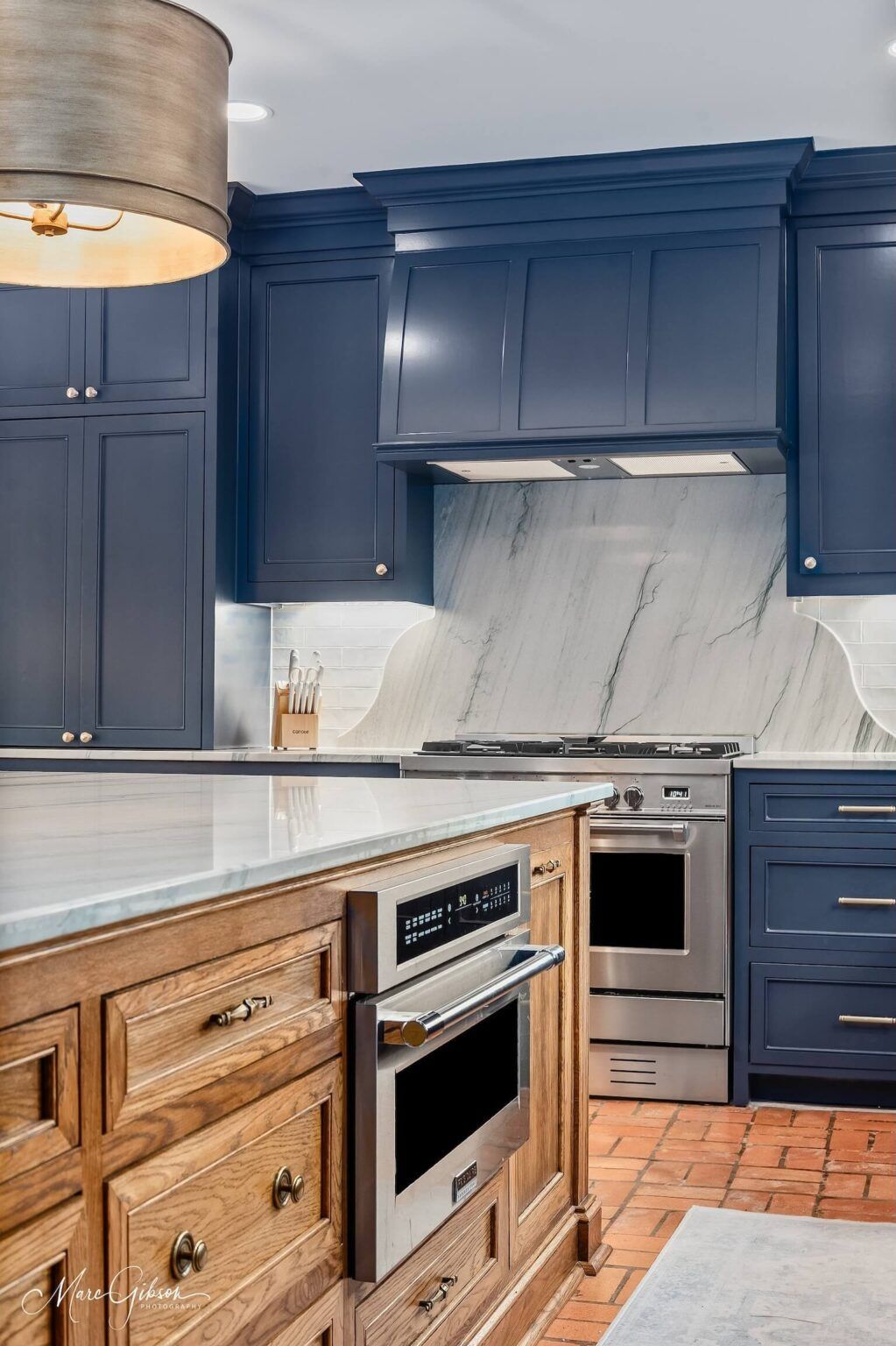 Blue kitchen with wood island, stainless oven, marble backsplash, and terracotta floor tiles