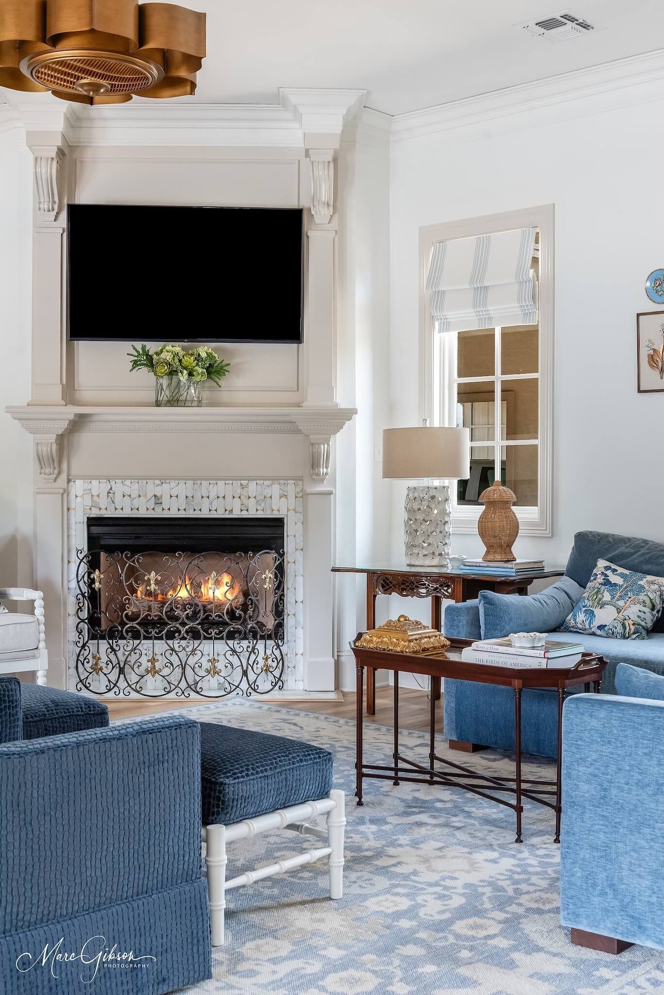Cozy living room with lit fireplace, wall-mounted TV, blue furniture, and decorative mirror