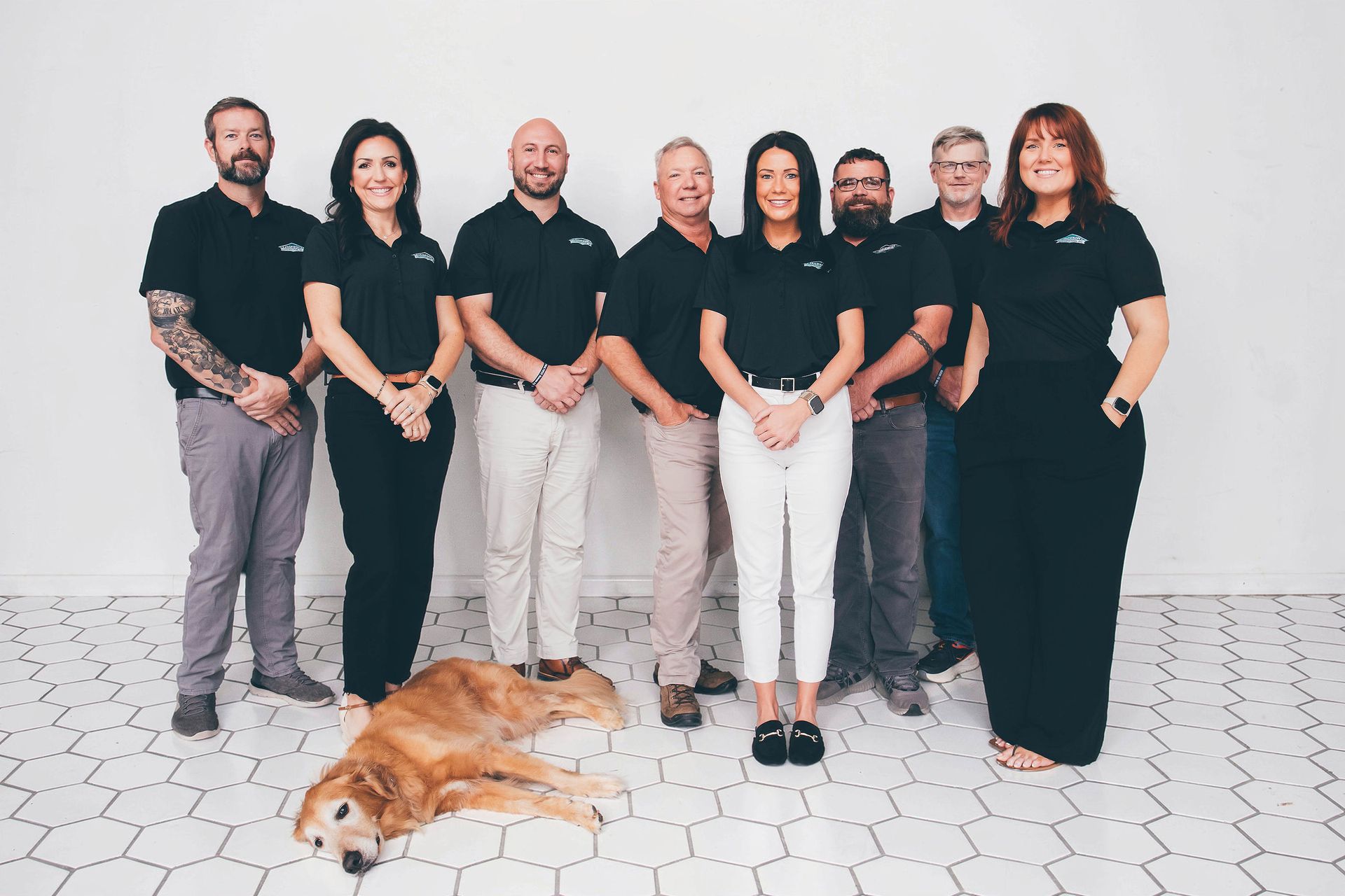 Seven people in black and white outfits posing indoors with a dog lying in front.