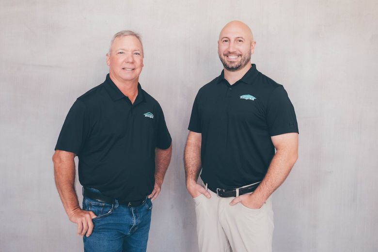 Two men in black polos posing against a light gray backdrop