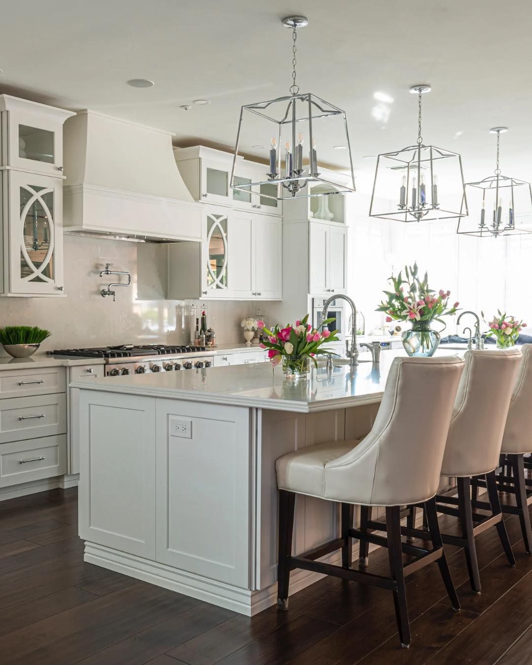 Bright white kitchen with island, bar stools, and pendant lights, decorated with flowers.