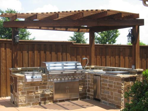 Outdoor brick grill and pergola in a backyard patio with wooden fence.