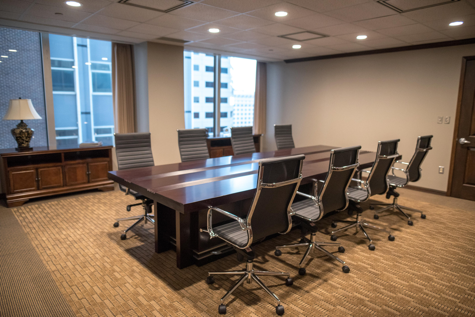 Modern conference room with long wooden table, black office chairs, and city view windows