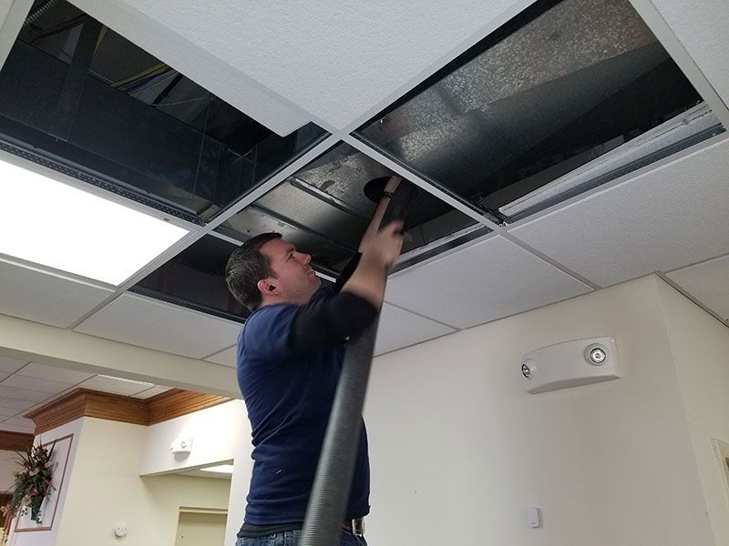 A man is cleaning the ceiling with a vacuum cleaner.