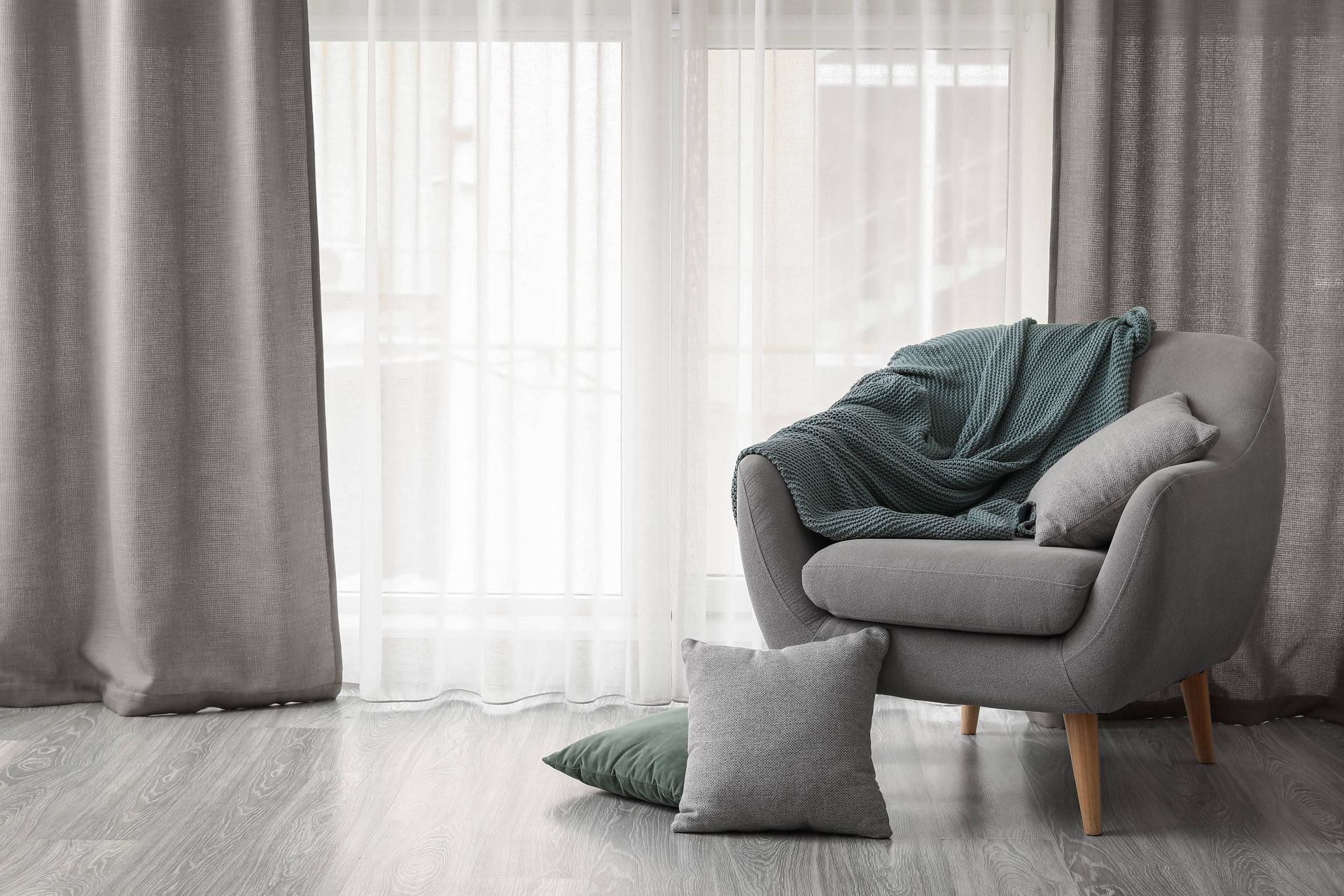 A living room with a chair , pillows , curtains and a window.