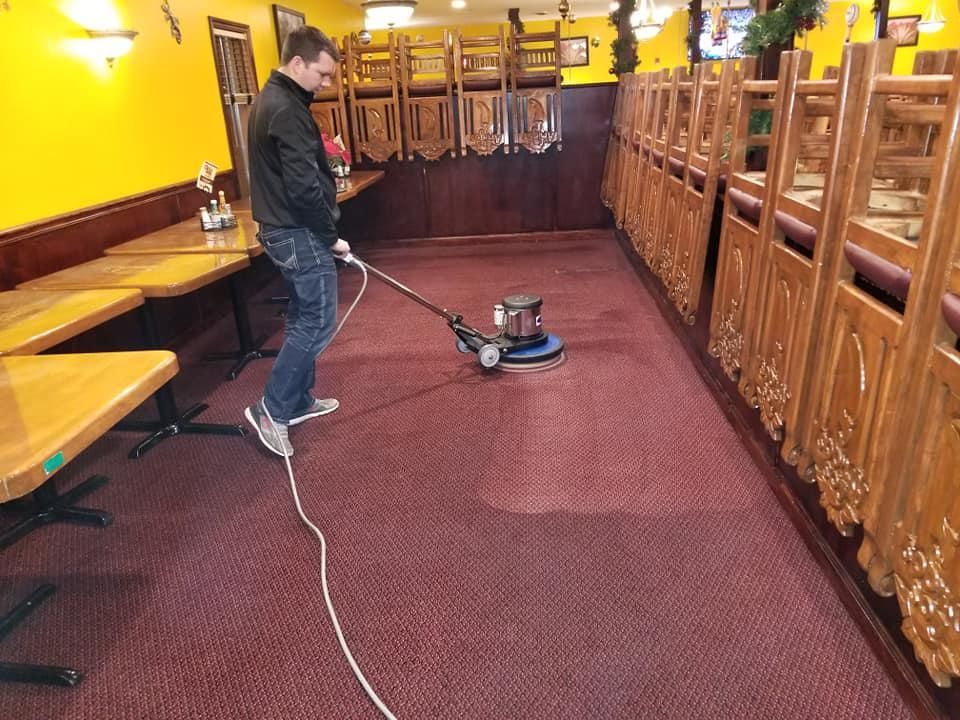 A man is using a machine to clean the carpet in a restaurant