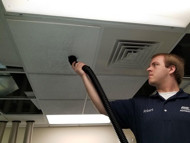 A man is using a vacuum cleaner to clean a ceiling