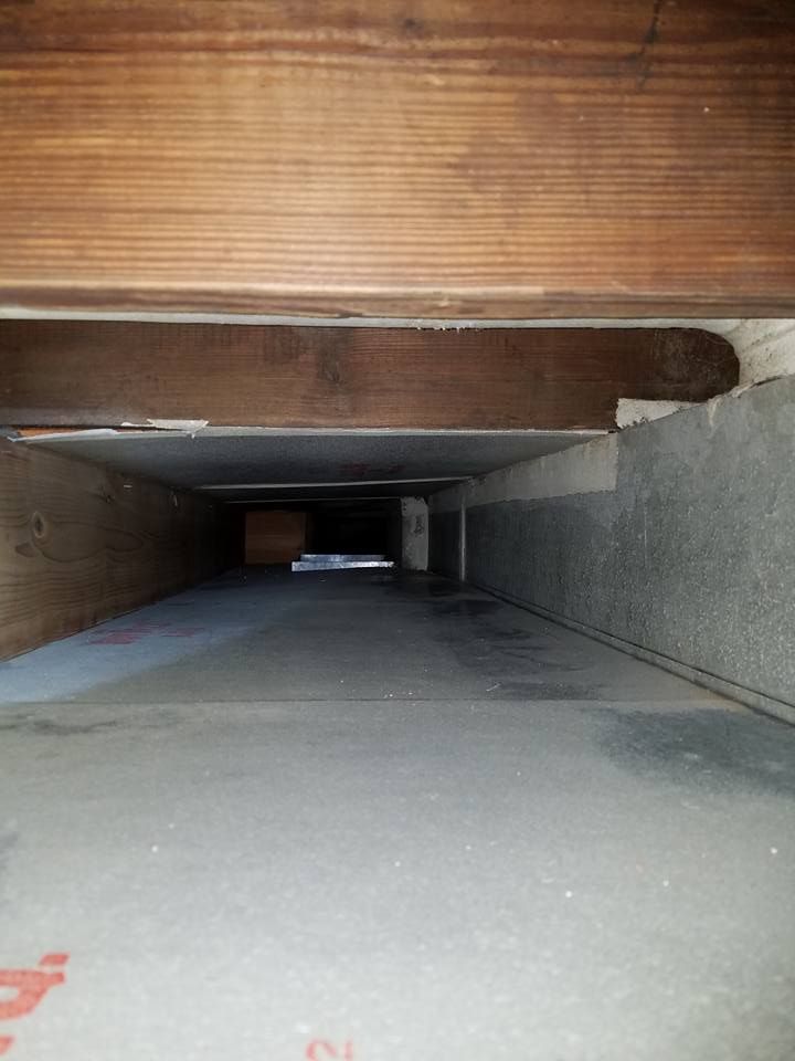 Looking down a narrow hallway with wooden beams and a concrete floor.