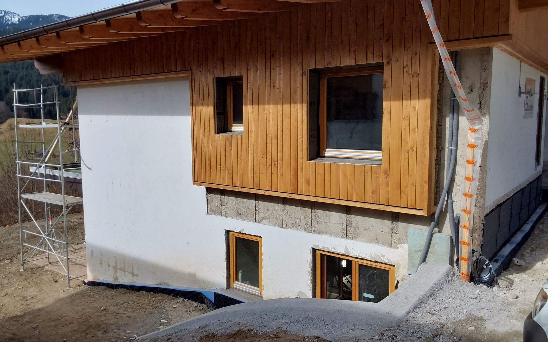 Haus im Bau: weißer Stuck, Holzverkleidung, Fenster, Gerüst und Entwässerungssystem.