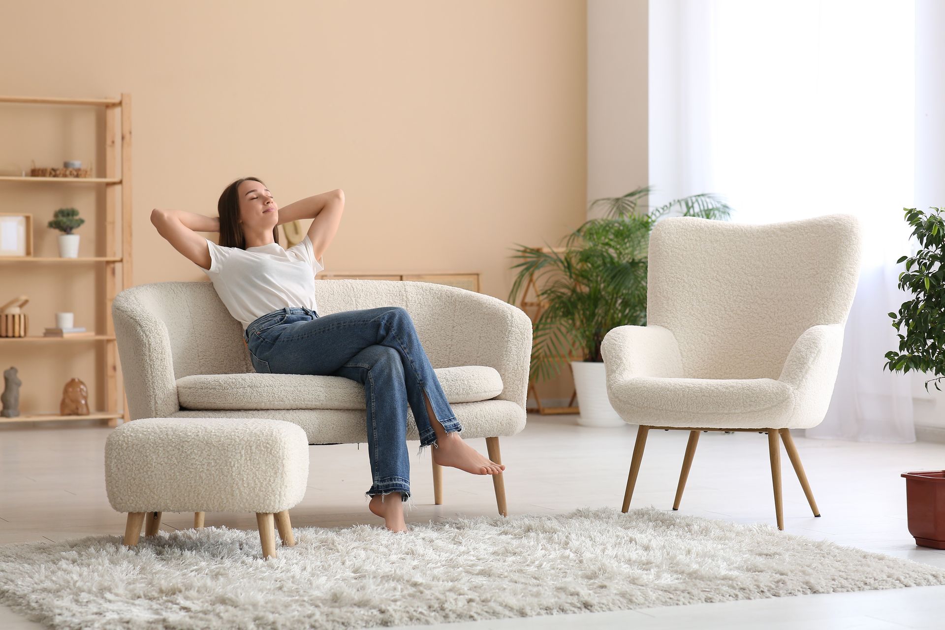 Frau entspannt sich auf einem cremefarbenen Sofa, die Hände hinter dem Kopf, in einem hellen, minimalistischen Wohnzimmer.