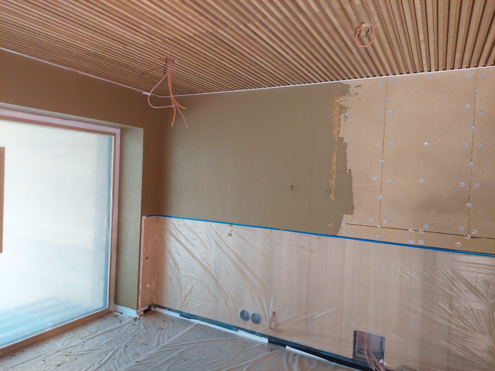 Zimmer im Umbau, mit braunen Wänden und Holzlattendecke. Plastikfolie bedeckt die untere Wand.