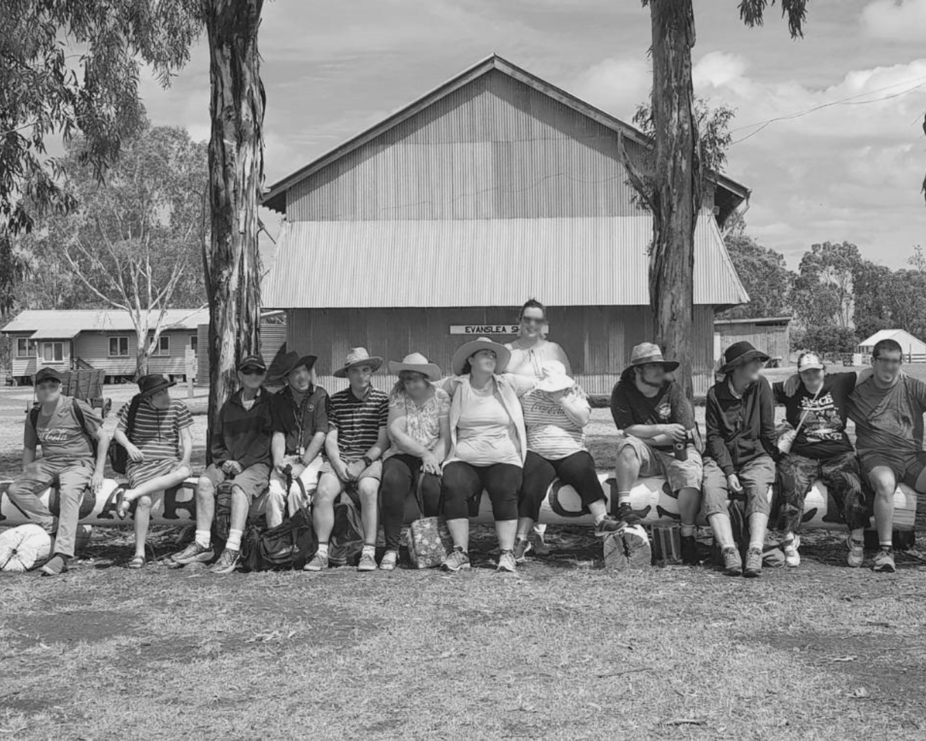 A group seated outdoors in front of a wooden building, posing together in a park-like setting.