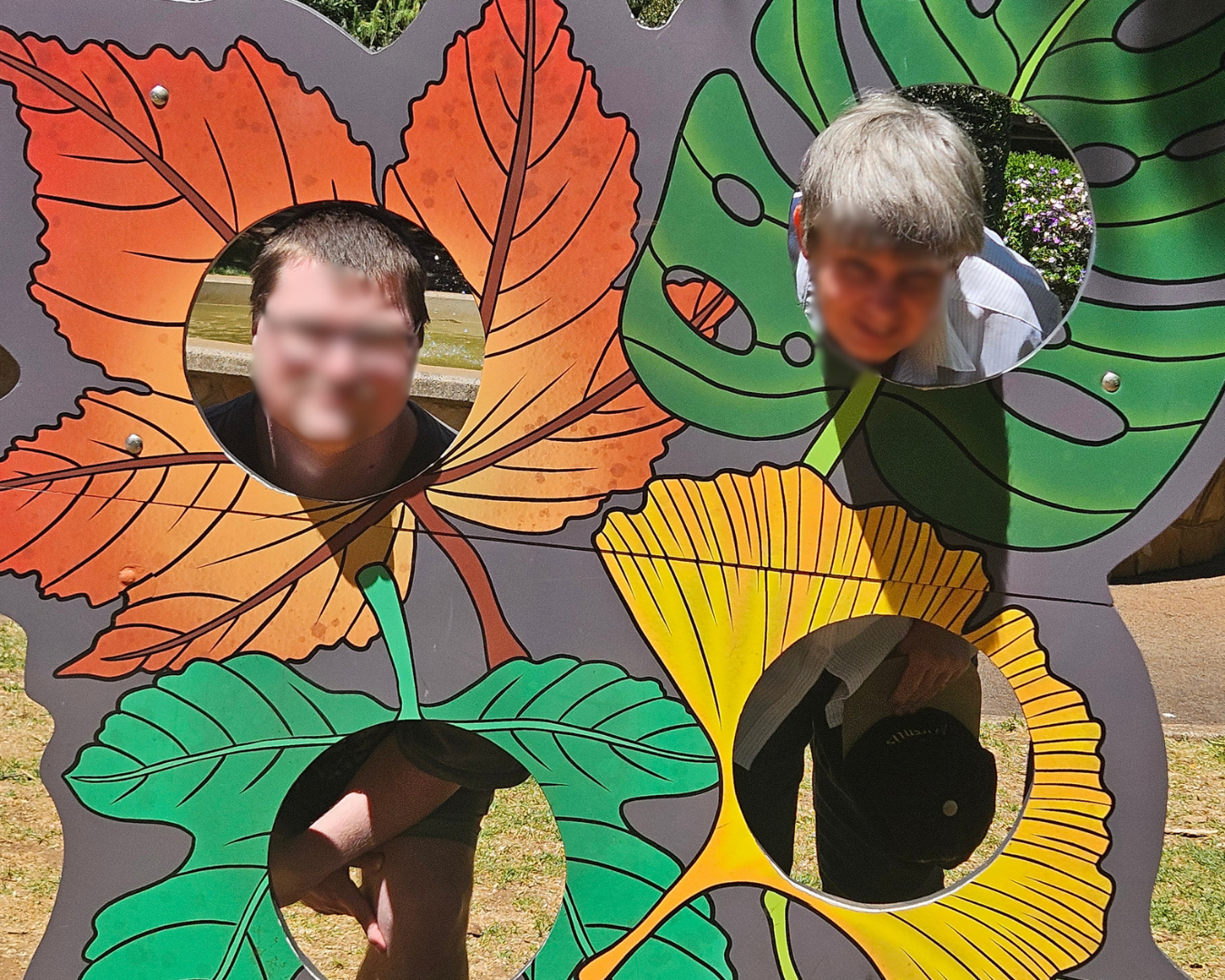 Colorful leaf cutout board with four face holes, showing people behind orange, green, and yellow leaves