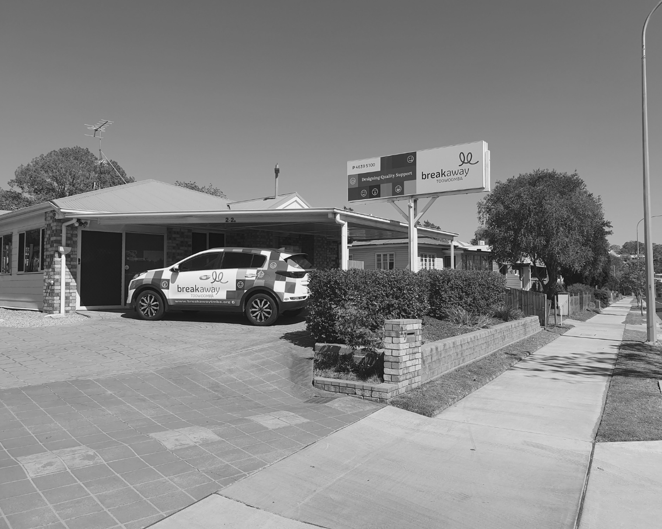 Police car parked in front of a low building on a sunny suburban sidewalk.