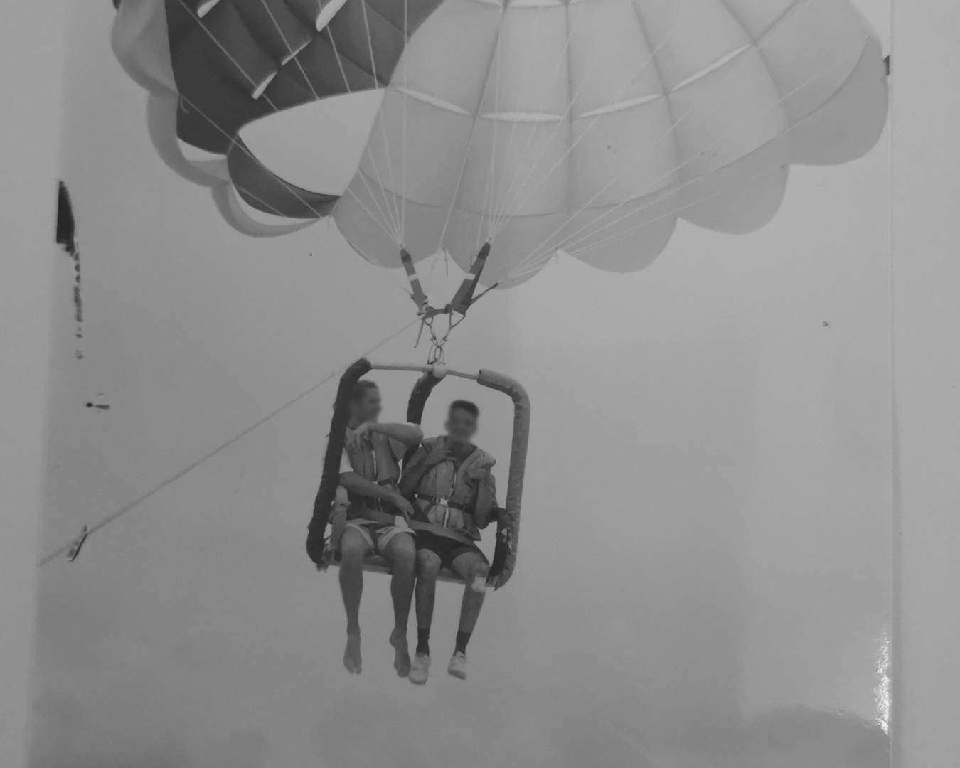 Two people parasailing beneath a large white canopy above the water