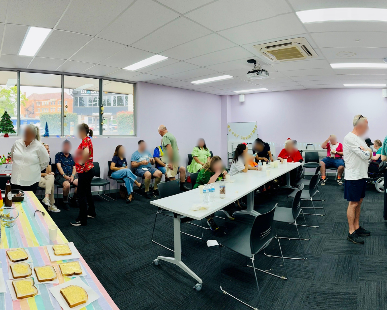 People seated around tables in a bright meeting room, chatting during a casual gathering.
