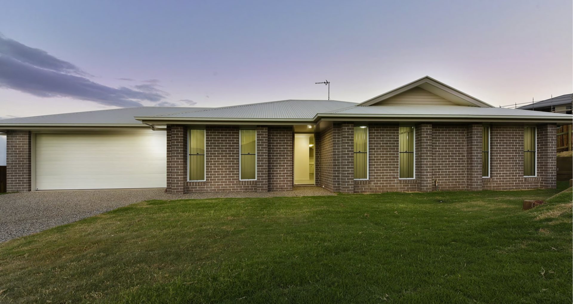 Single-story brick house with a garage and front lawn at dusk