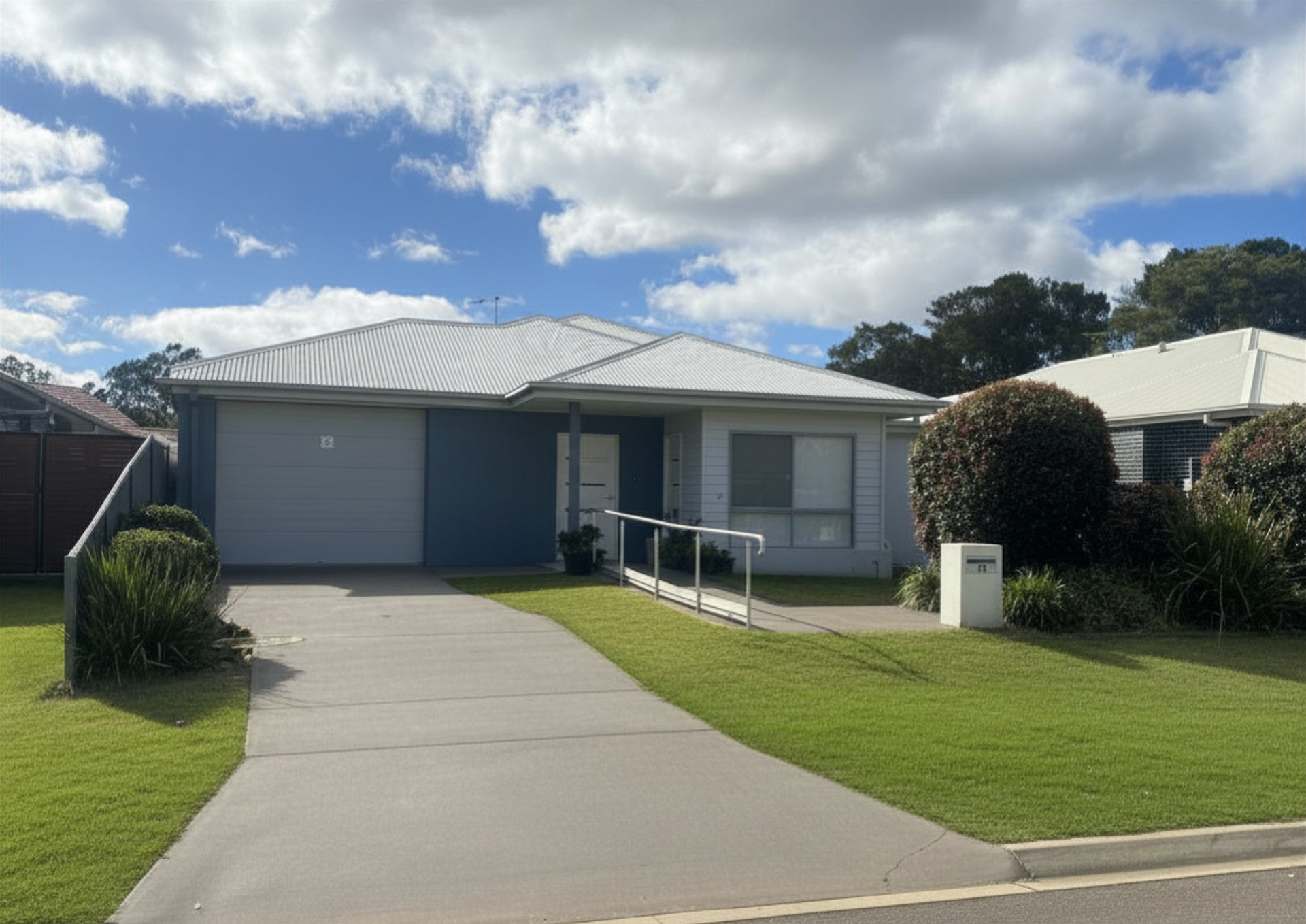 Single-story suburban house with a driveway, lawn, and blue sky with clouds