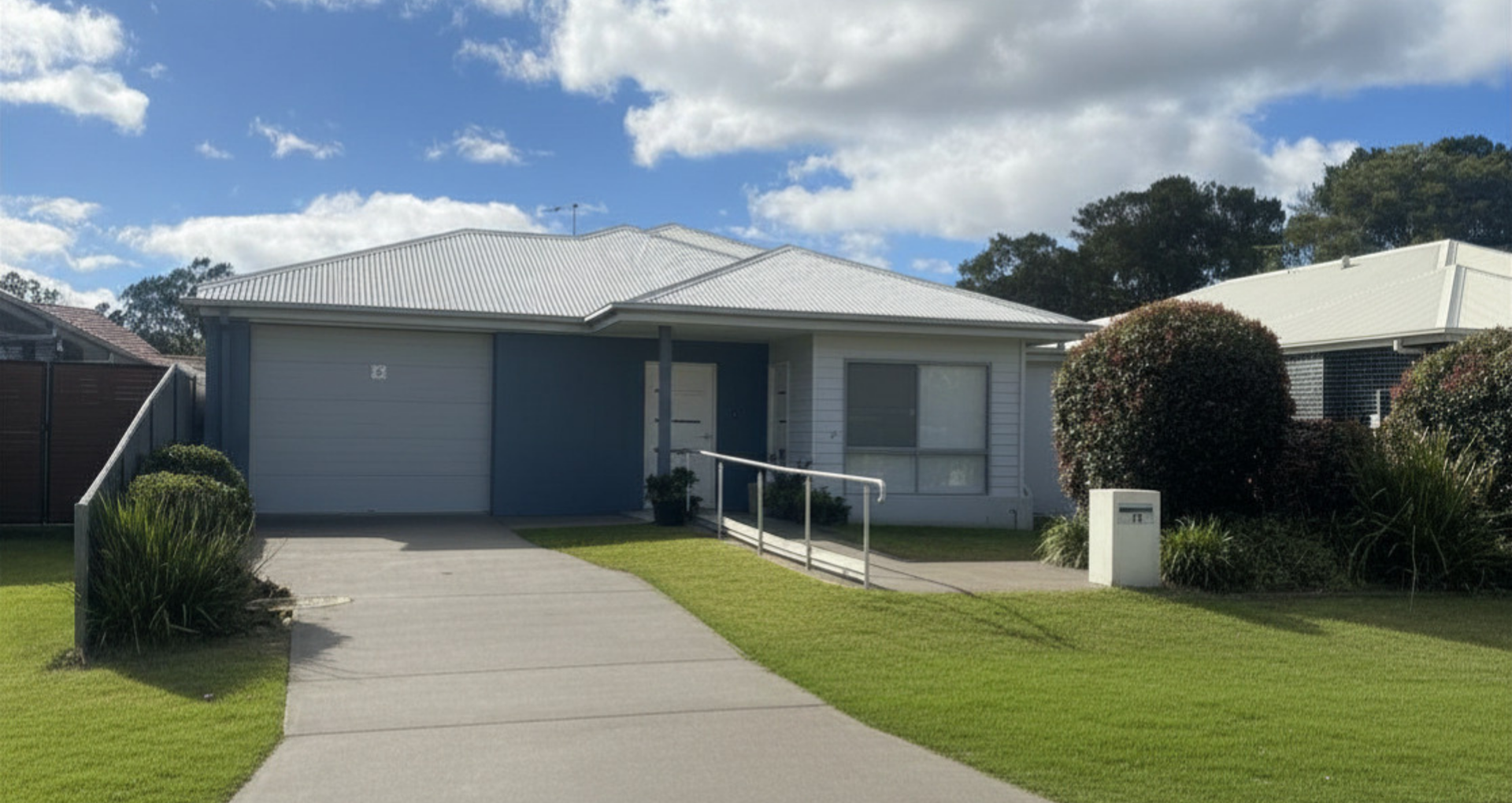 Single-story blue house with driveway, lawn, and front ramp under a cloudy sky