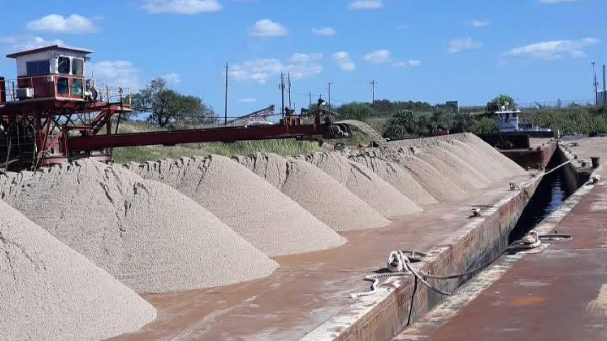 Industrial site with large white gravel piles lined along a conveyor or loading area under a blue sky