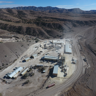 Aerial view of a dusty construction site in a desert valley, with buildings, roads, and mountains nearby