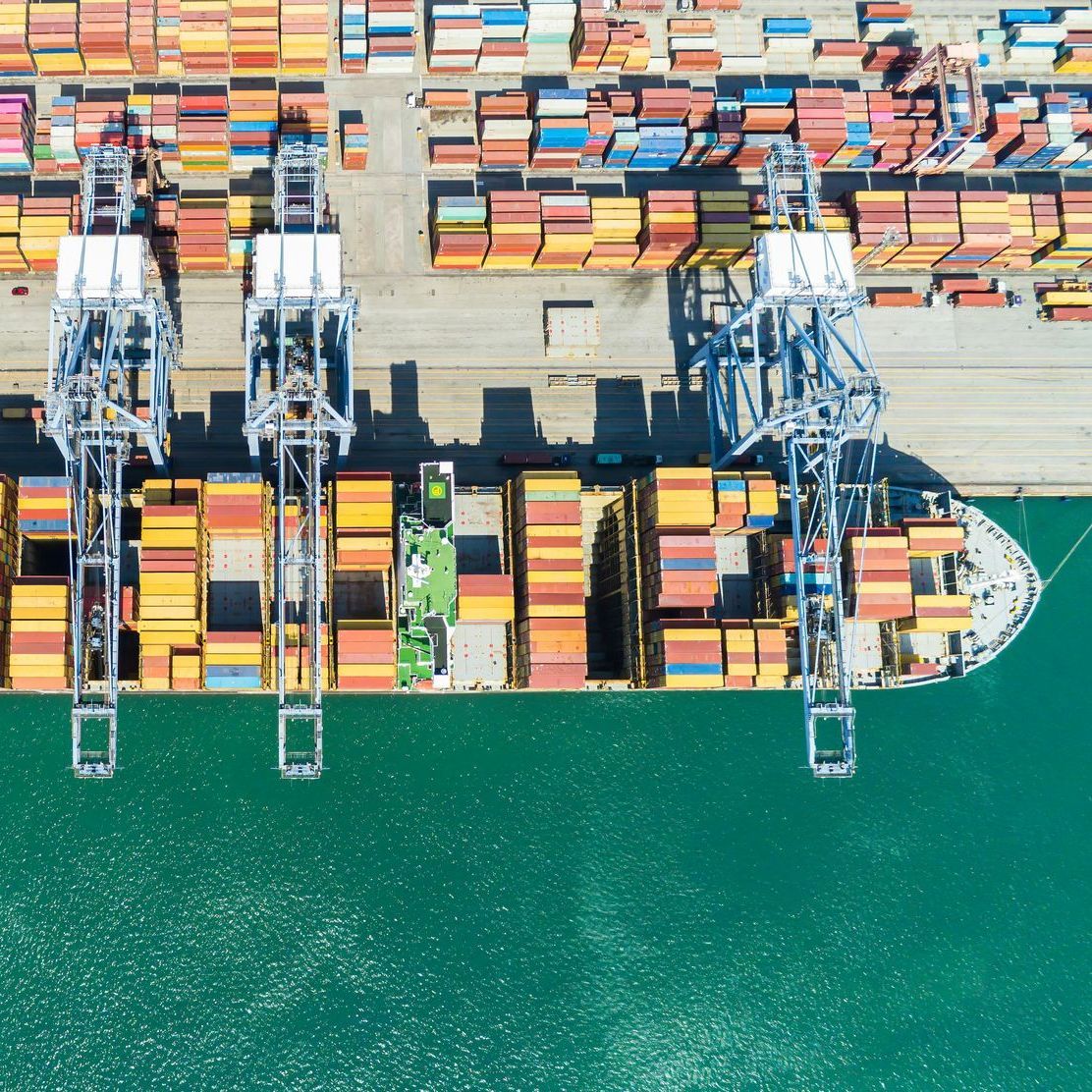 Aerial view of a container ship docked at port beside colorful stacked cargo and cranes
