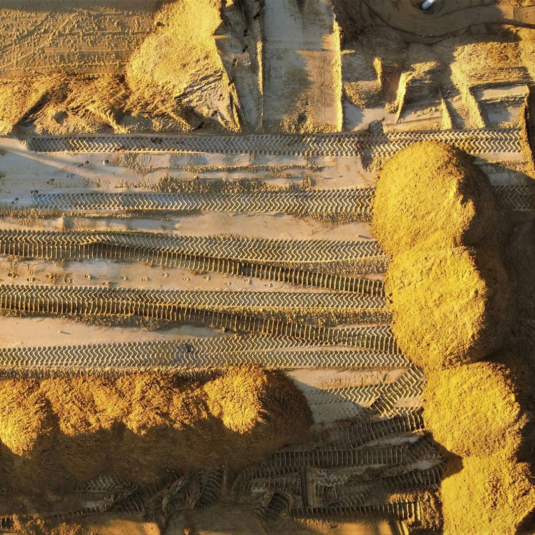 Golden hay bales and rows of cut grain in a sunlit field, viewed from above