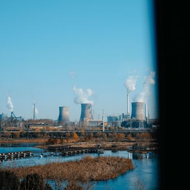 Industrial power plant with smoking cooling towers beside a blue river and marshland under a clear sky