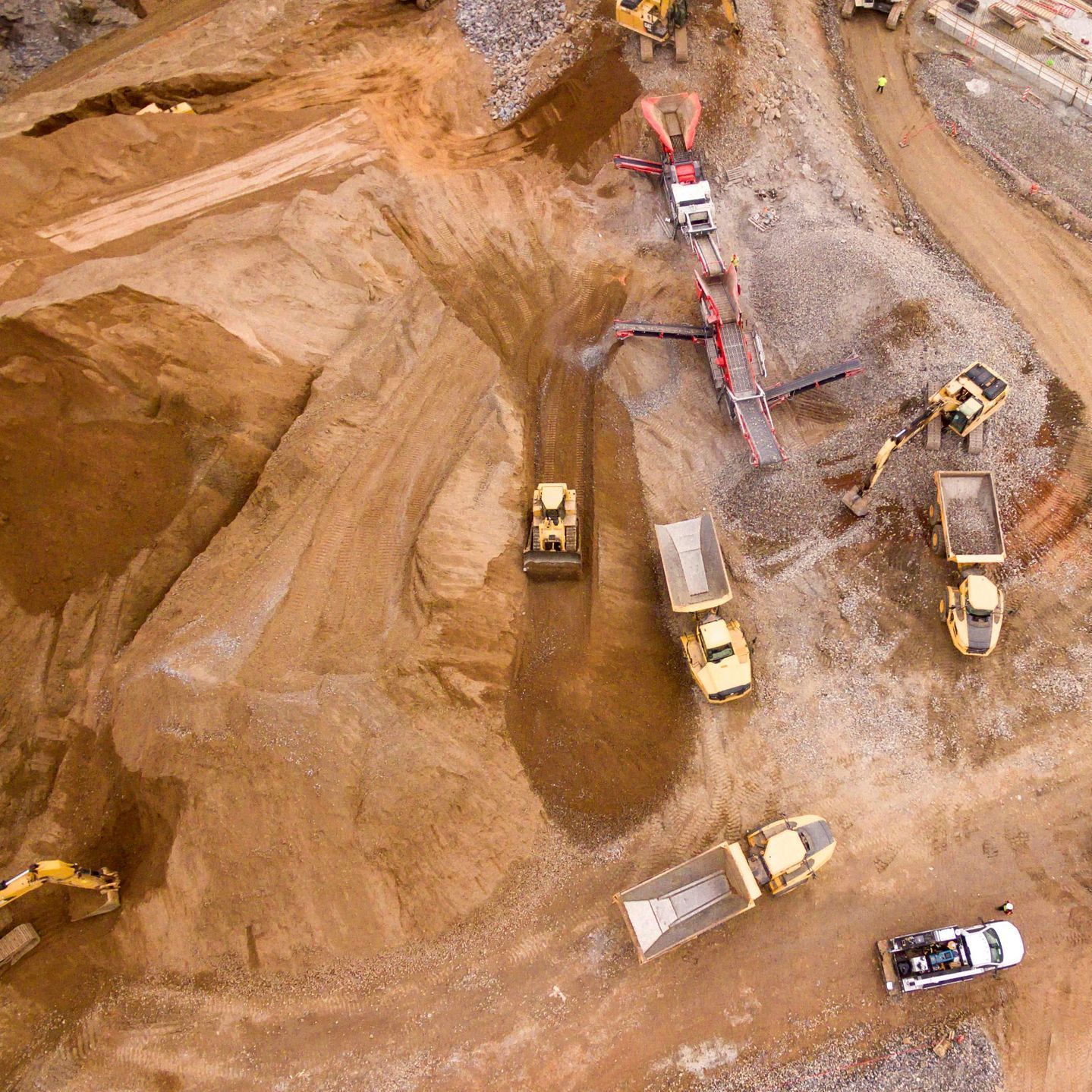 Aerial view of a construction site with several yellow bulldozers and dump trucks on dirt roads.
