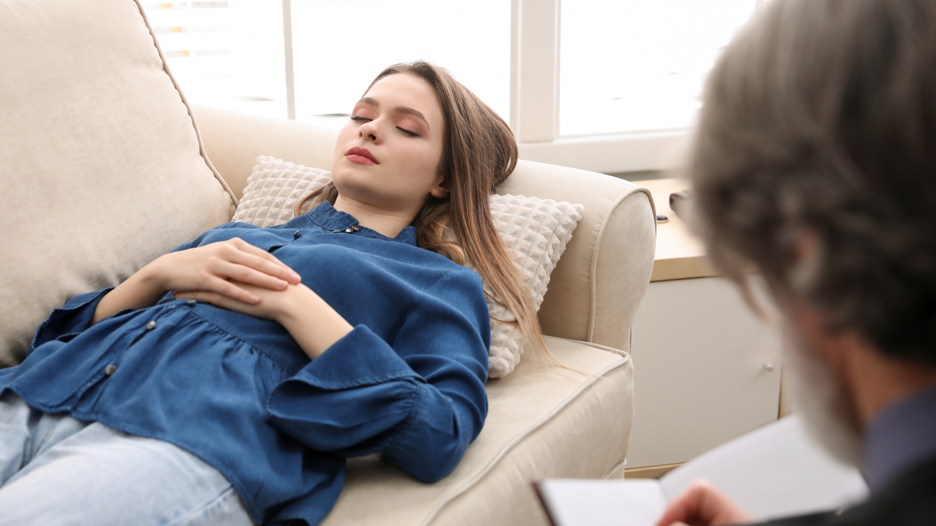 Person reclining on a couch during a therapy session while a counselor listens nearby
