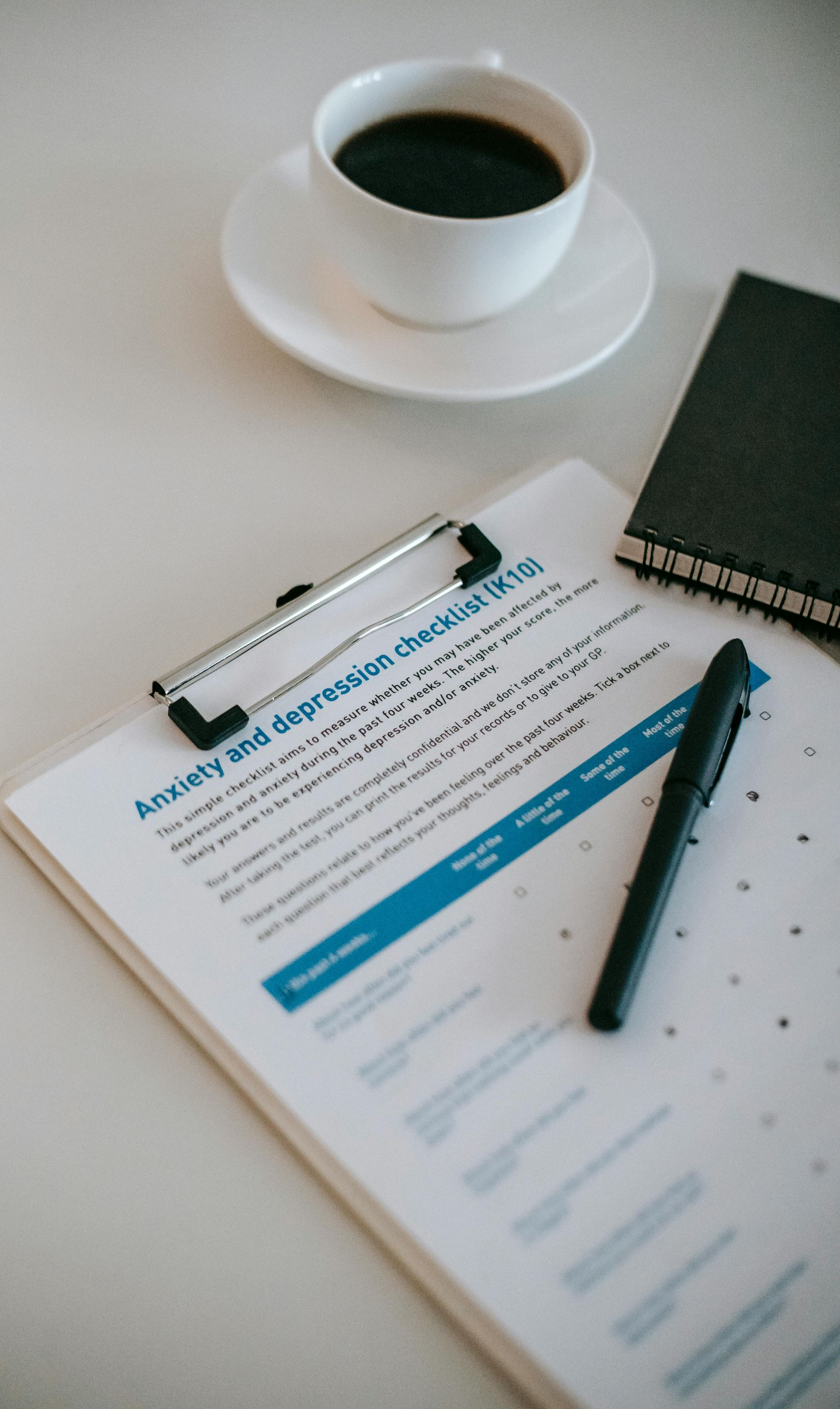 Coffee cup, clipboard with form, pen, and notebook on a white desk