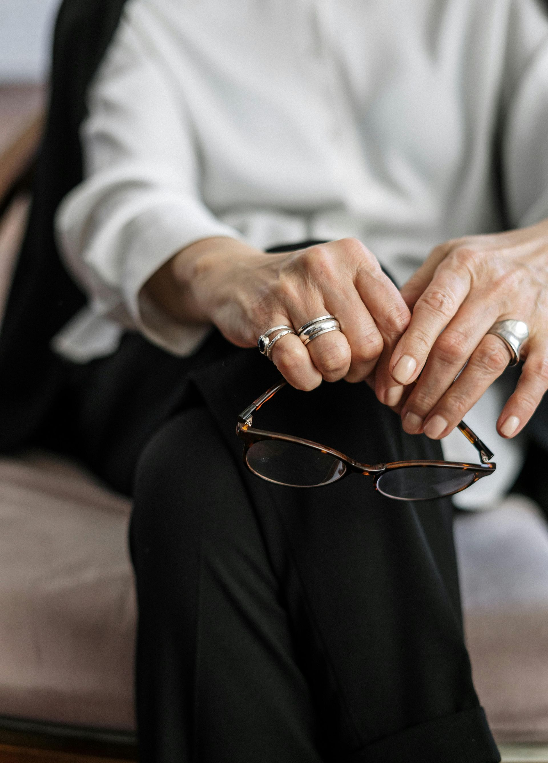 Hands holding eyeglasses over crossed black-clad legs on a couch