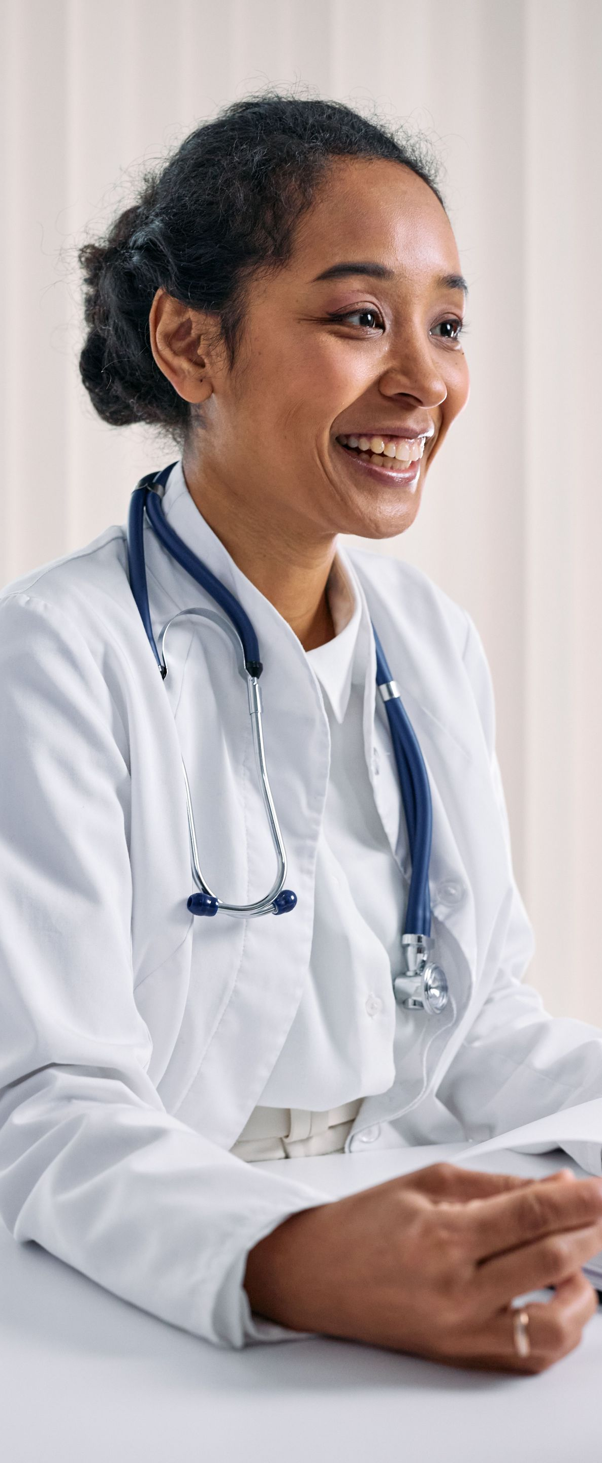 Smiling medical professional in a white coat and stethoscope, seated and holding a clipboard.