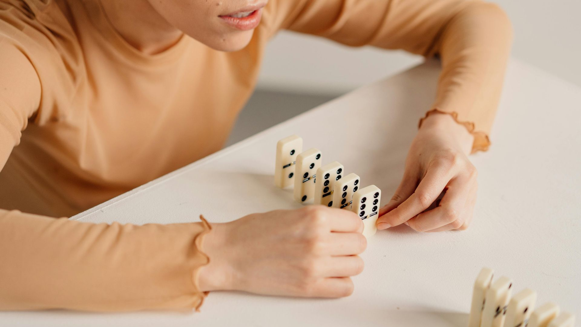 Person arranging dominoes on a white table with a wooden toy in the foreground