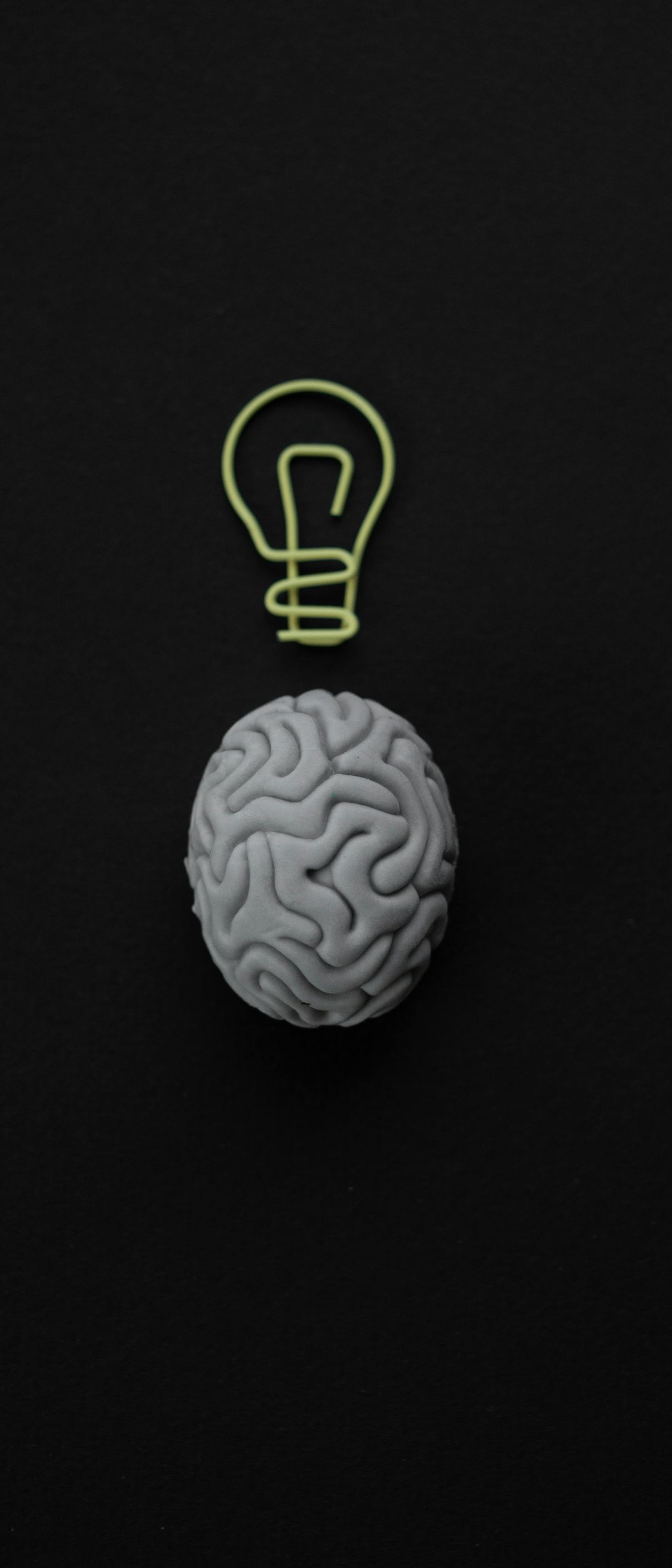 Gray brain under a yellow lightbulb on a dark background, symbolizing an idea.