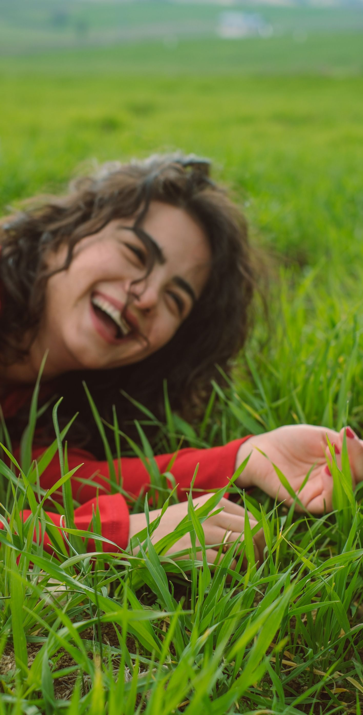 Smiling woman in a red top lying in green grass outdoors