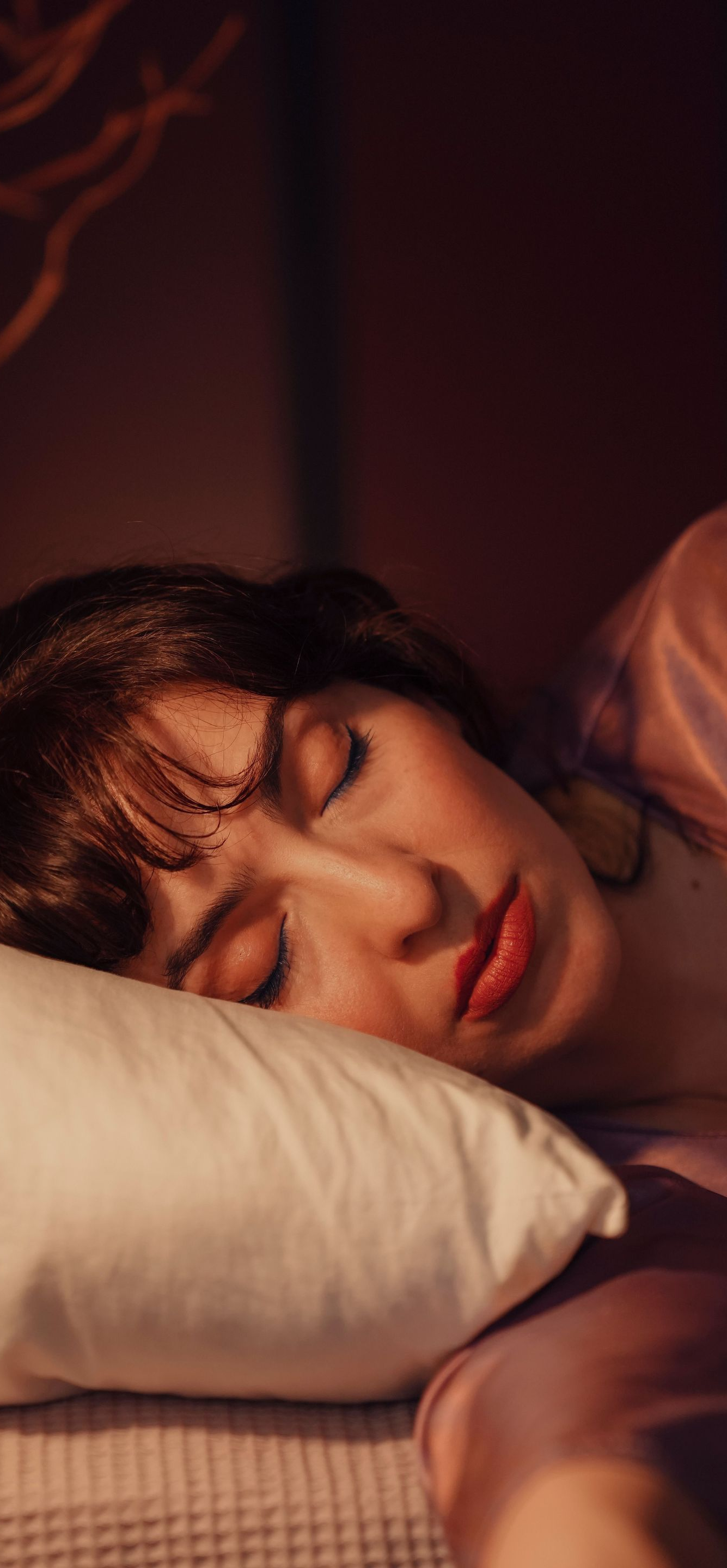 Woman sleeping on a white pillow in warm, dim light