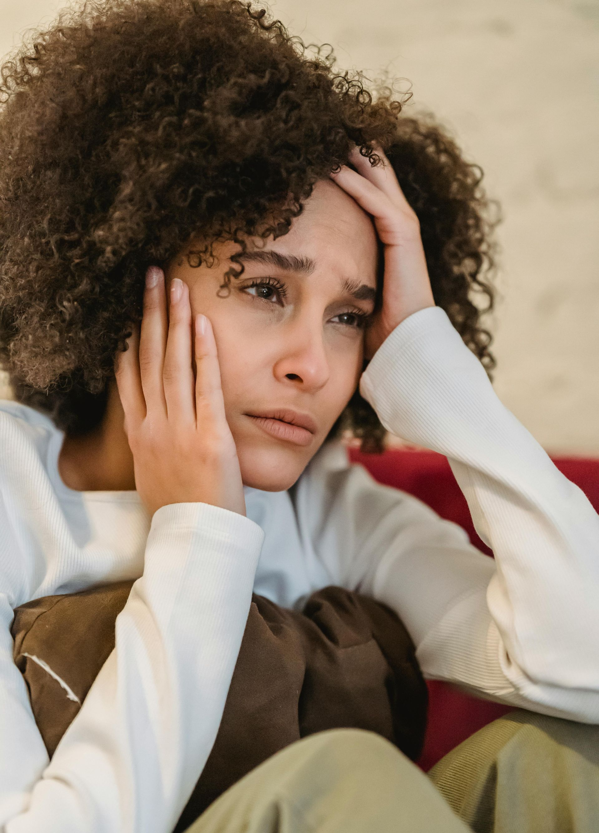 Person sitting with hands on face, looking worried, wearing a white sweater and brown vest.
