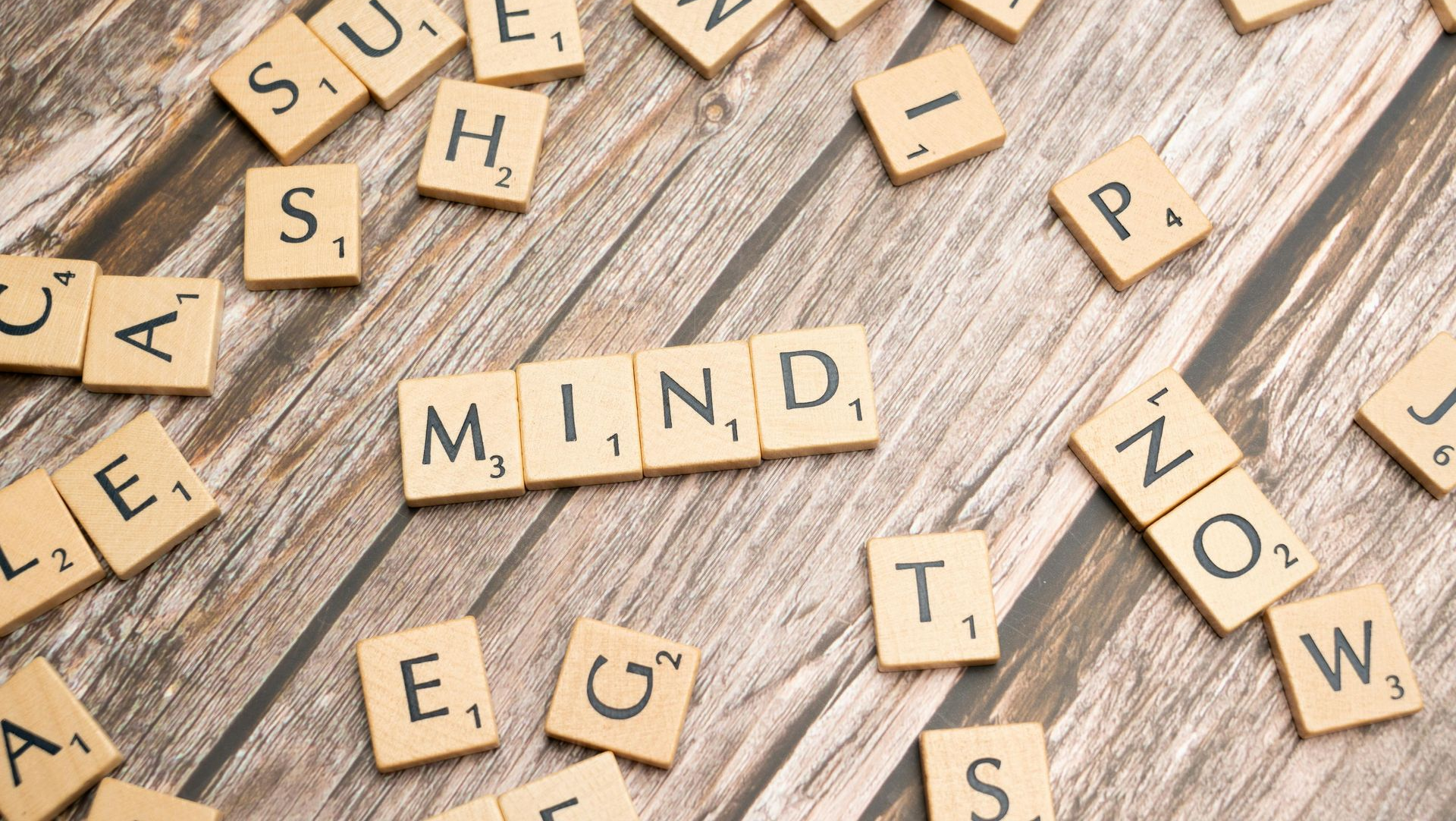 Scrabble tiles spelling “mind” and other scattered words on a wooden surface