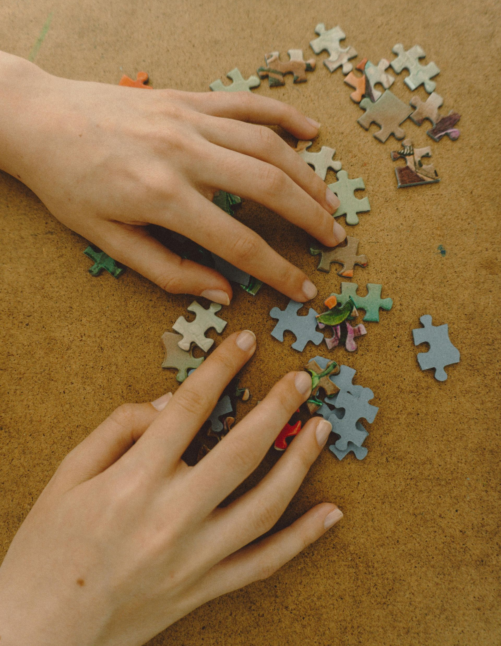 Hands sorting puzzle pieces on a brown surface