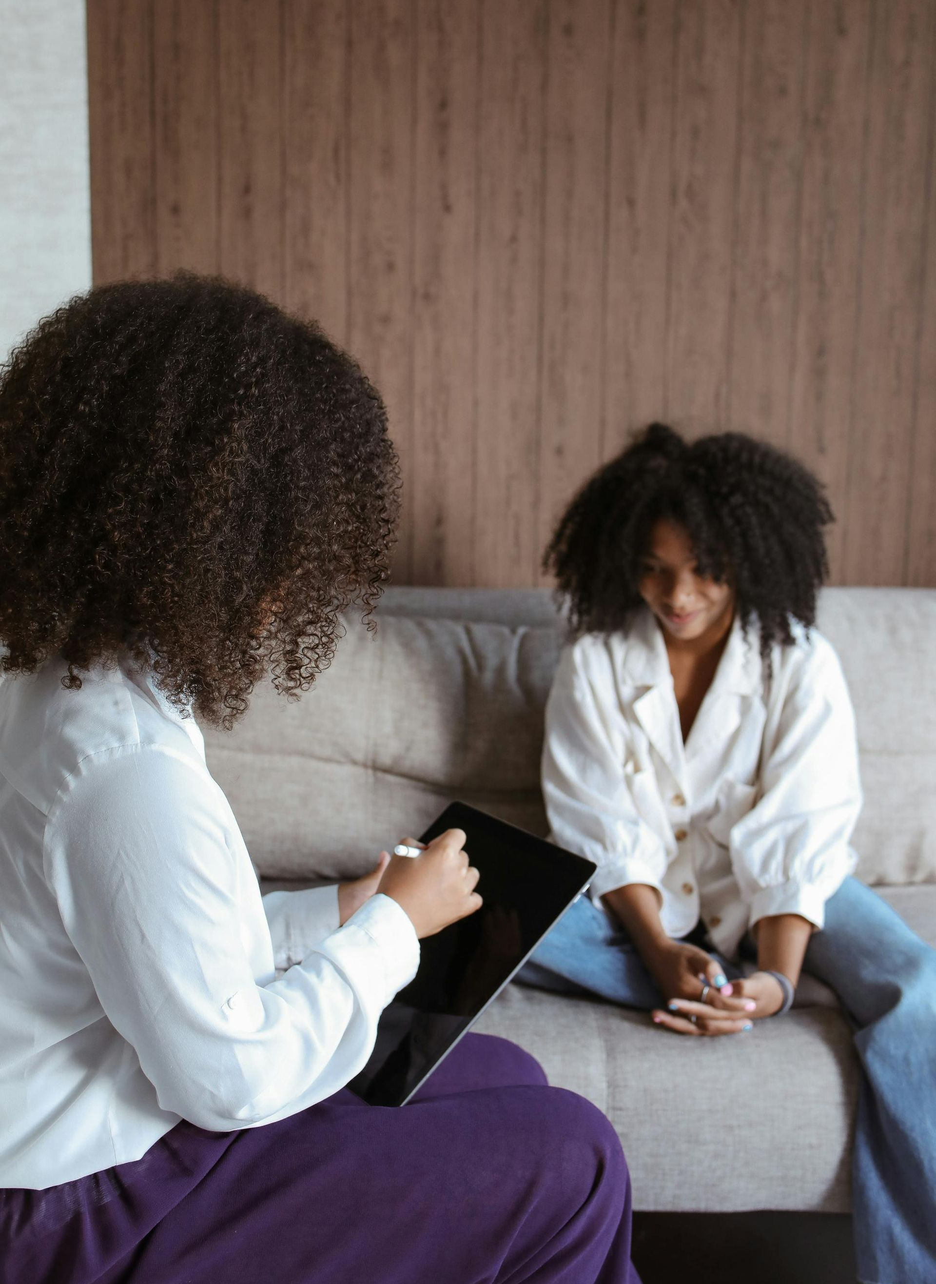 Two people seated on a sofa in a living room, talking while one holds a tablet.