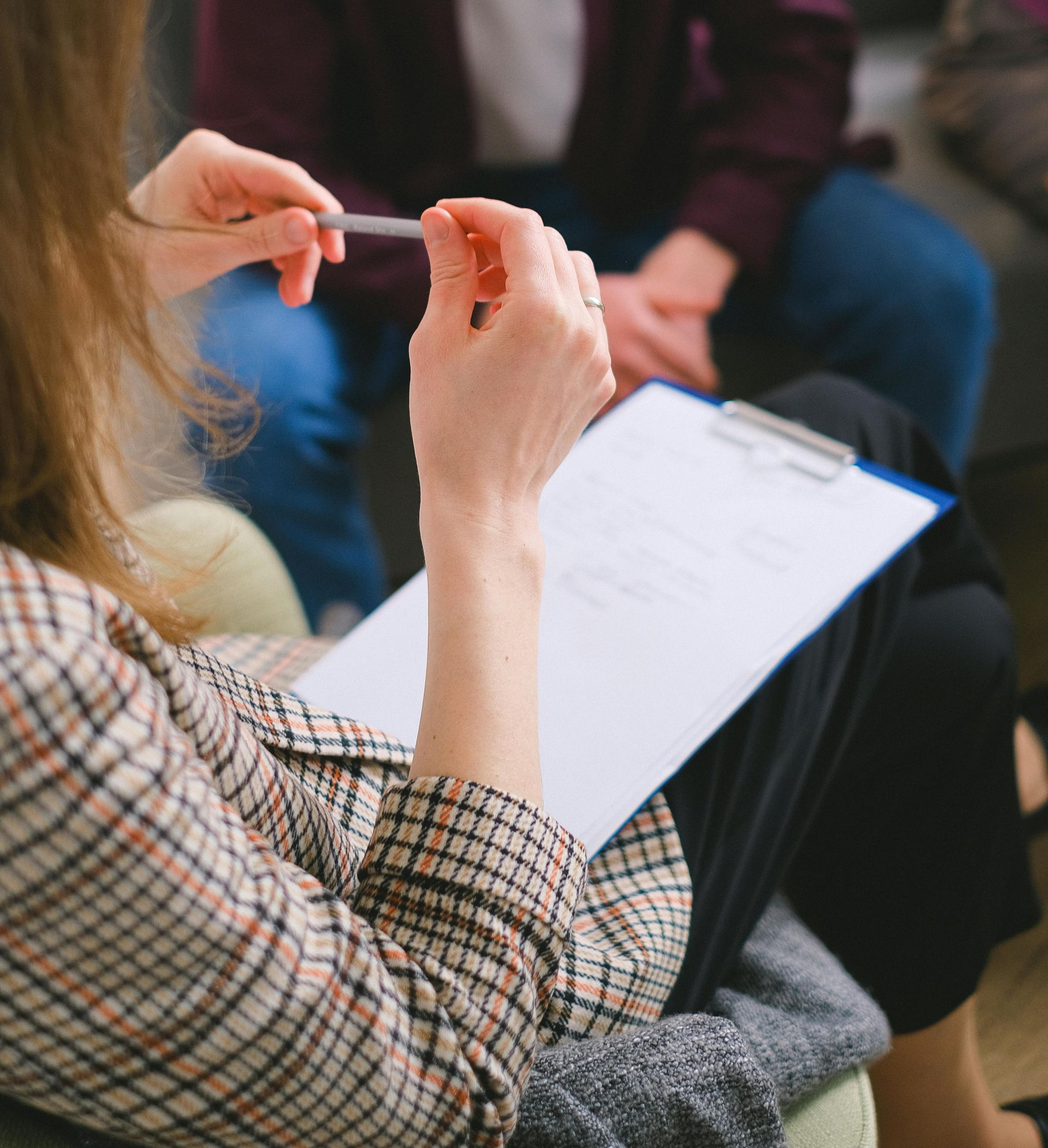 People in a group discussion, one holding a clipboard and pen in the foreground