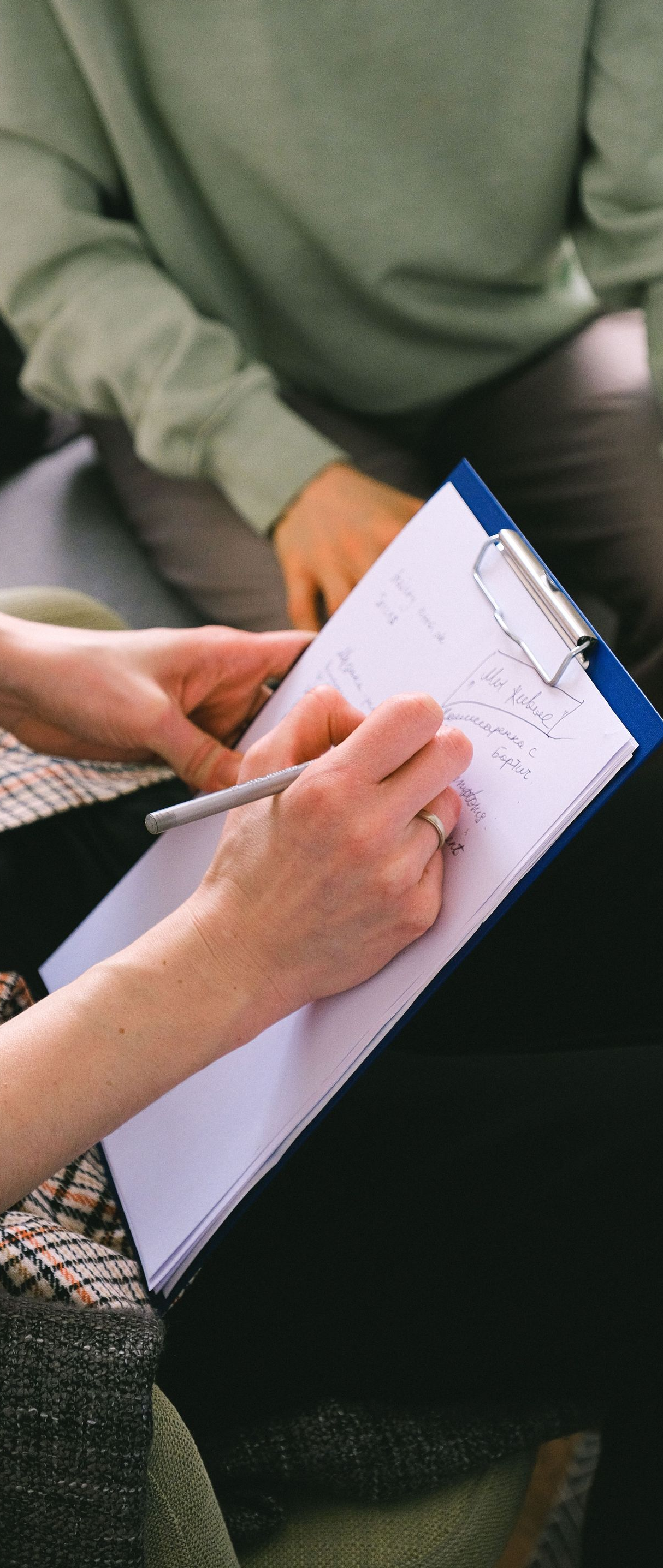 Hands taking notes on a clipboard during a meeting