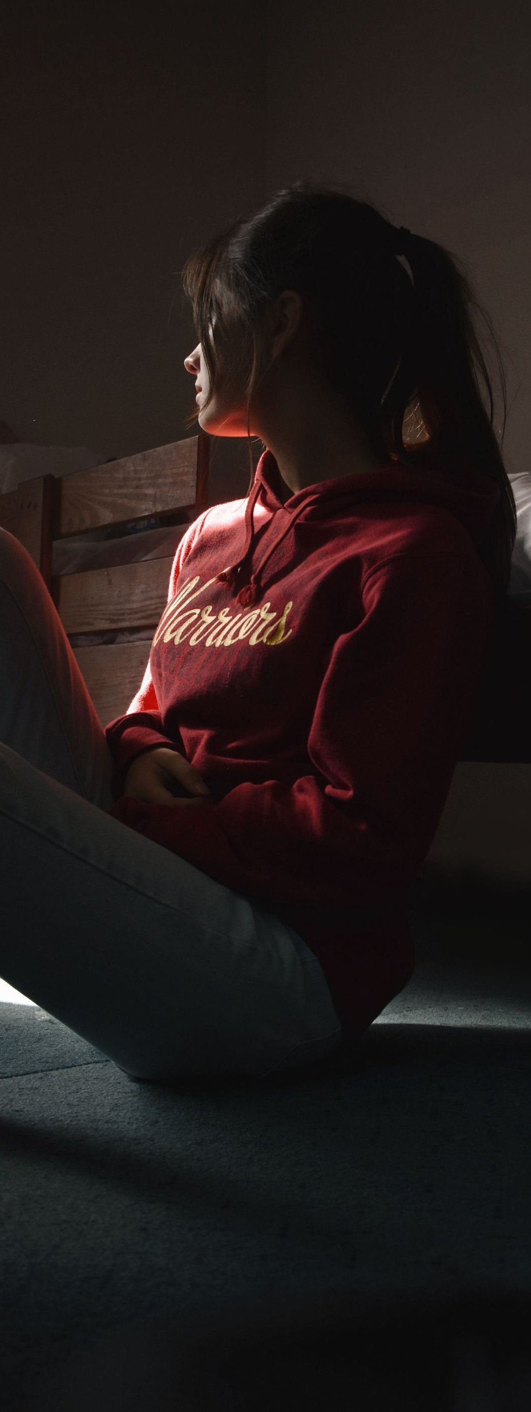 Person sitting in profile by a window, wearing a red top in dim light