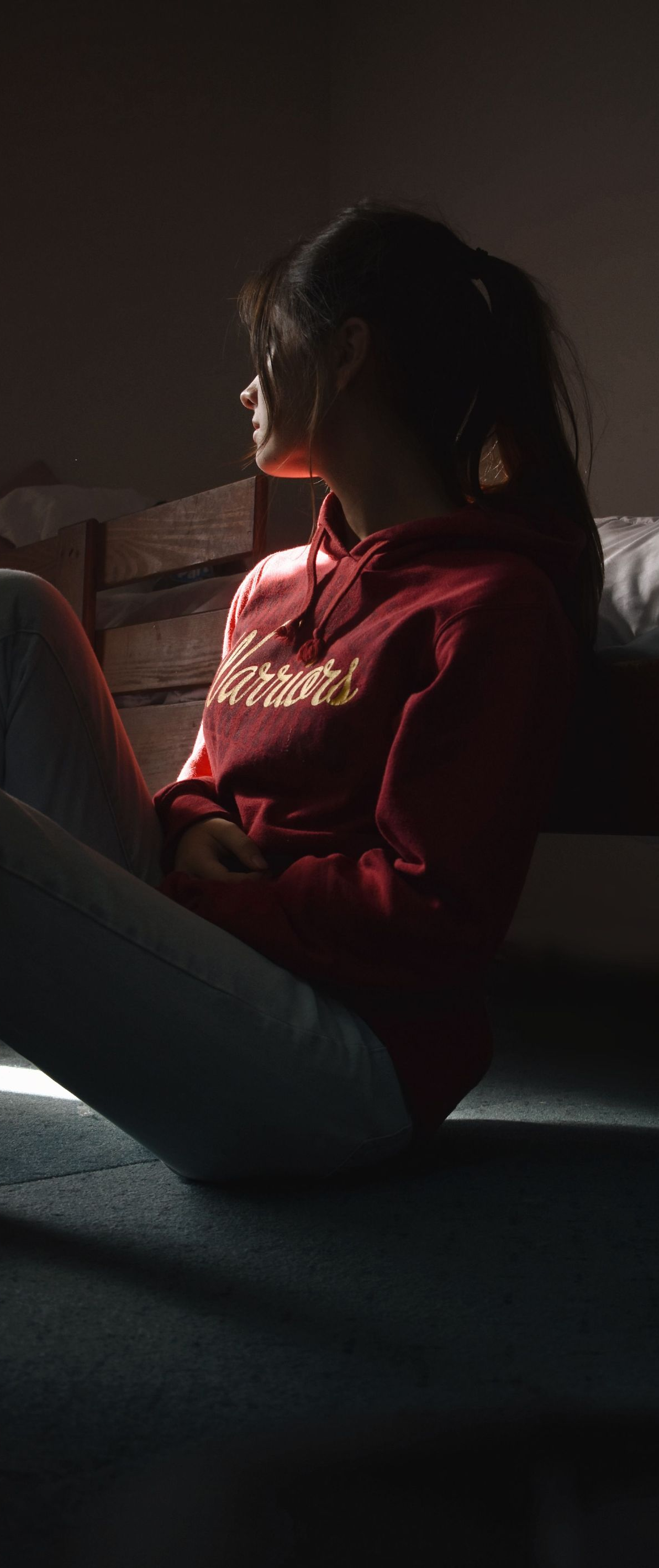 Person in a red shirt sitting in profile by a window, lit by soft sunlight.