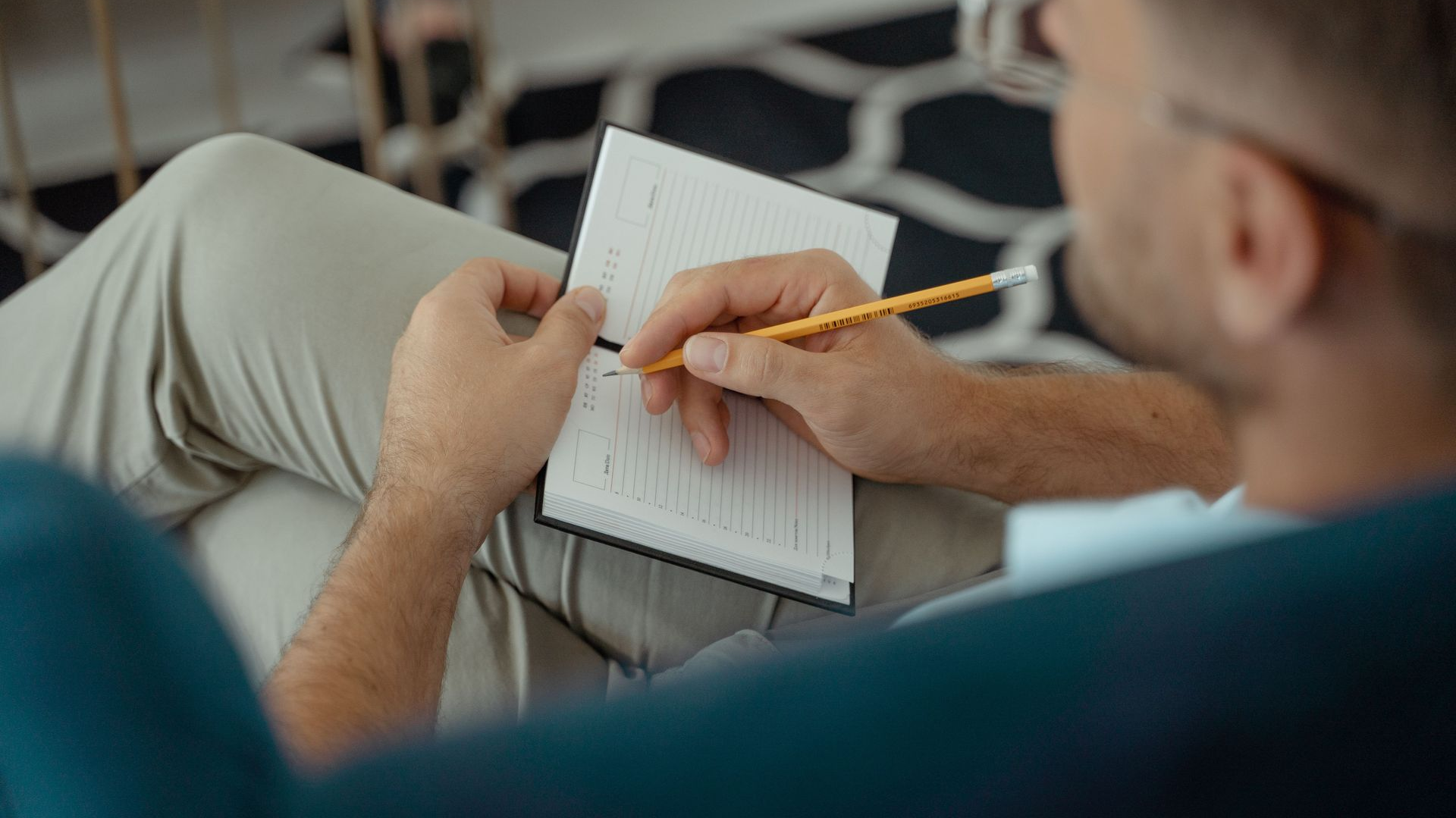 Person writing in a notebook with a pencil while seated on a couch