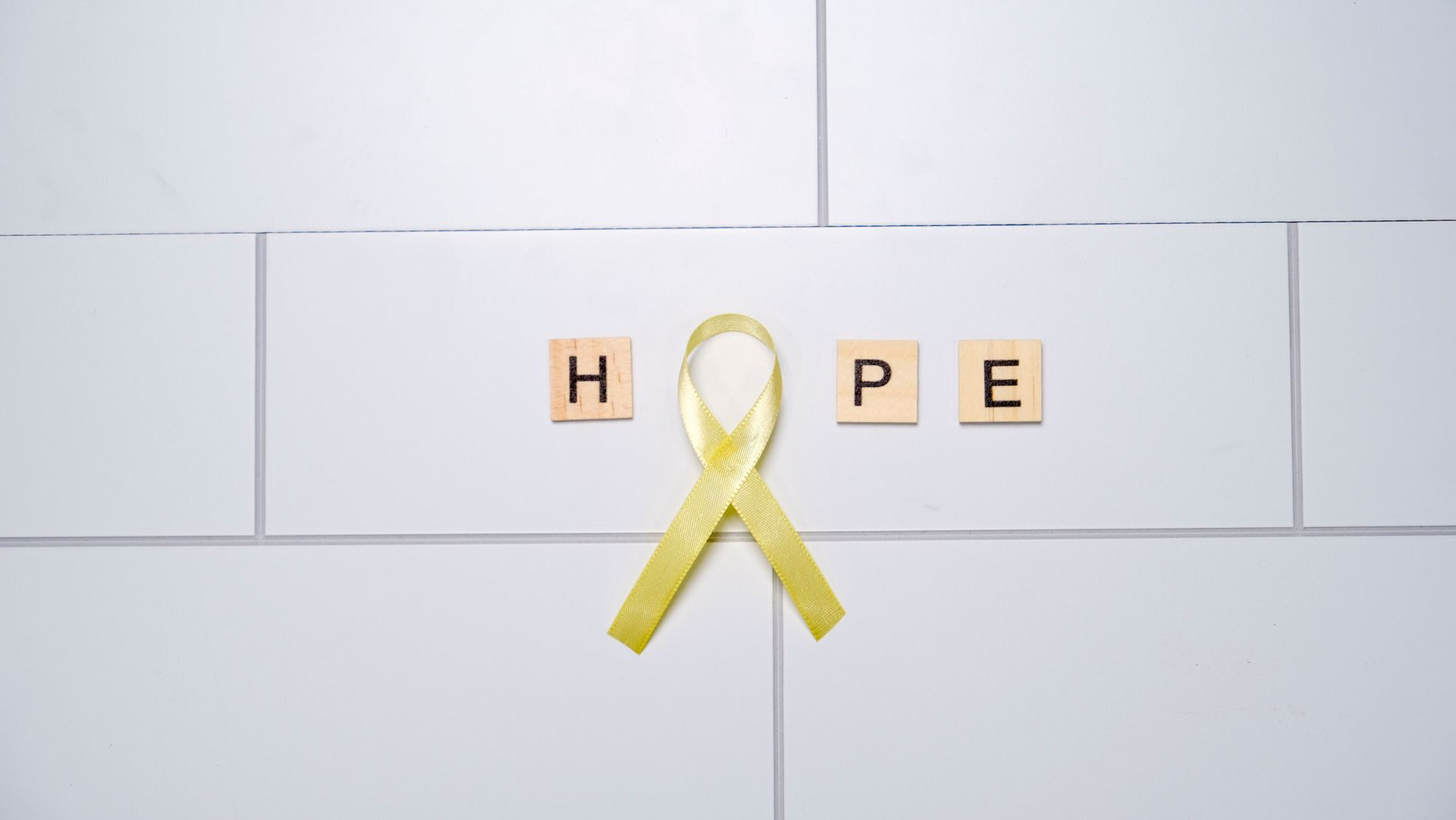 Yellow ribbon with “H O P E” tiles on a light brick wall.