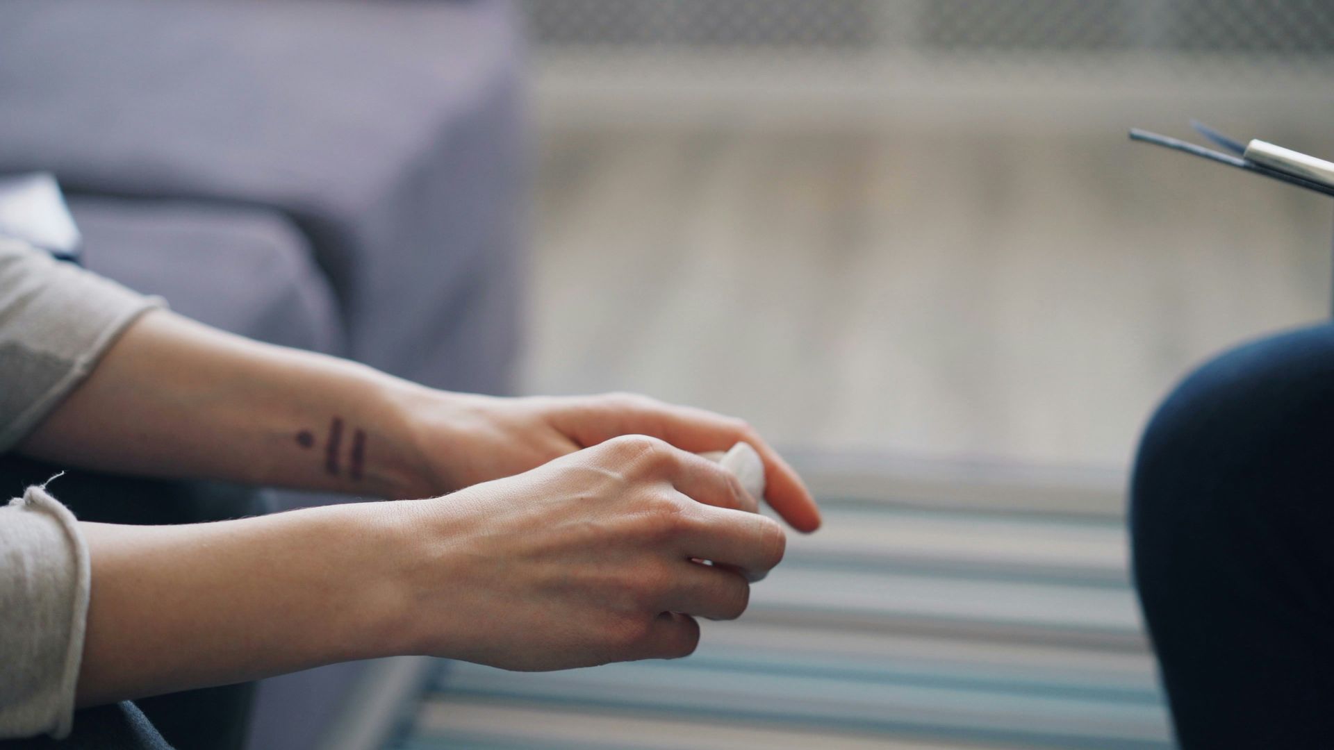 Hands resting near a window, with a dark chair or person’s leg at right.