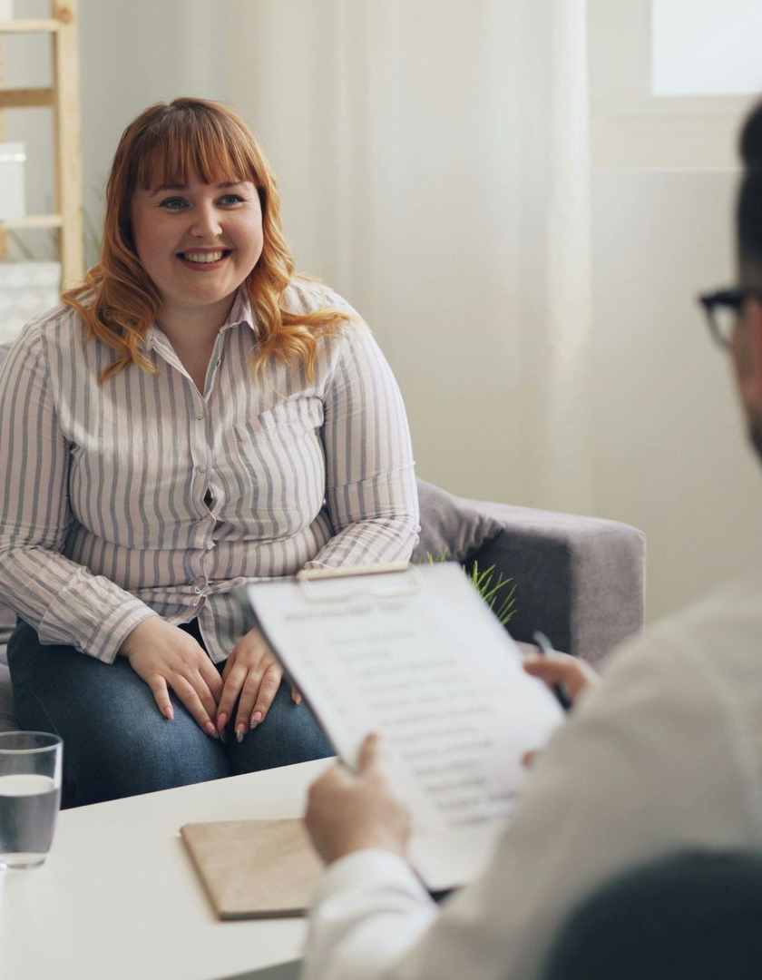 Smiling woman in a striped shirt during a counseling session, facing a therapist across a table.